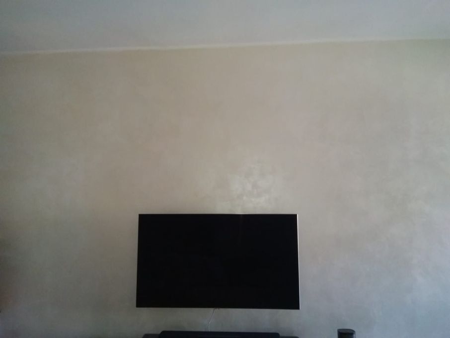 Un televisore nero montato a parete su una parete testurizzata beige chiaro. La parete è sopra un mobile scuro.