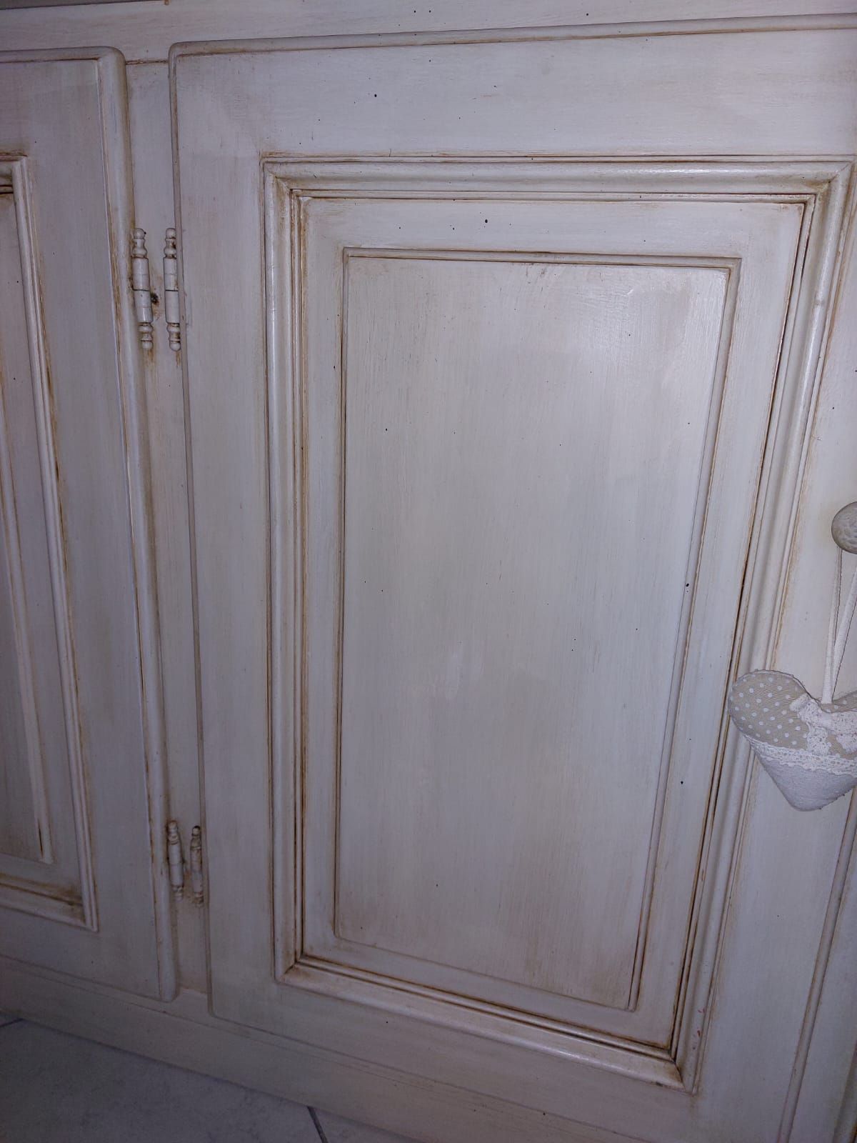 Mobile bianco con finitura anticata, caratterizzato da pannelli delle ante rettangolari con dettagli più scuri.