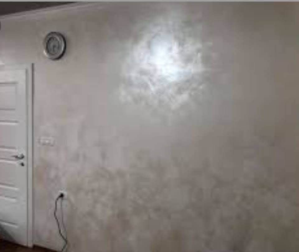 Una parete con finitura perlescente e testurizzata. Sono visibili una porta bianca e un orologio.