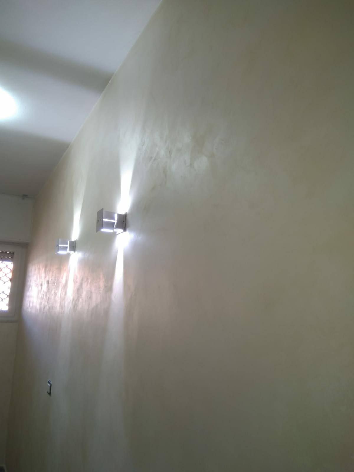 Parete color crema con tre applique moderne che proiettano una luce intensa verso il basso.