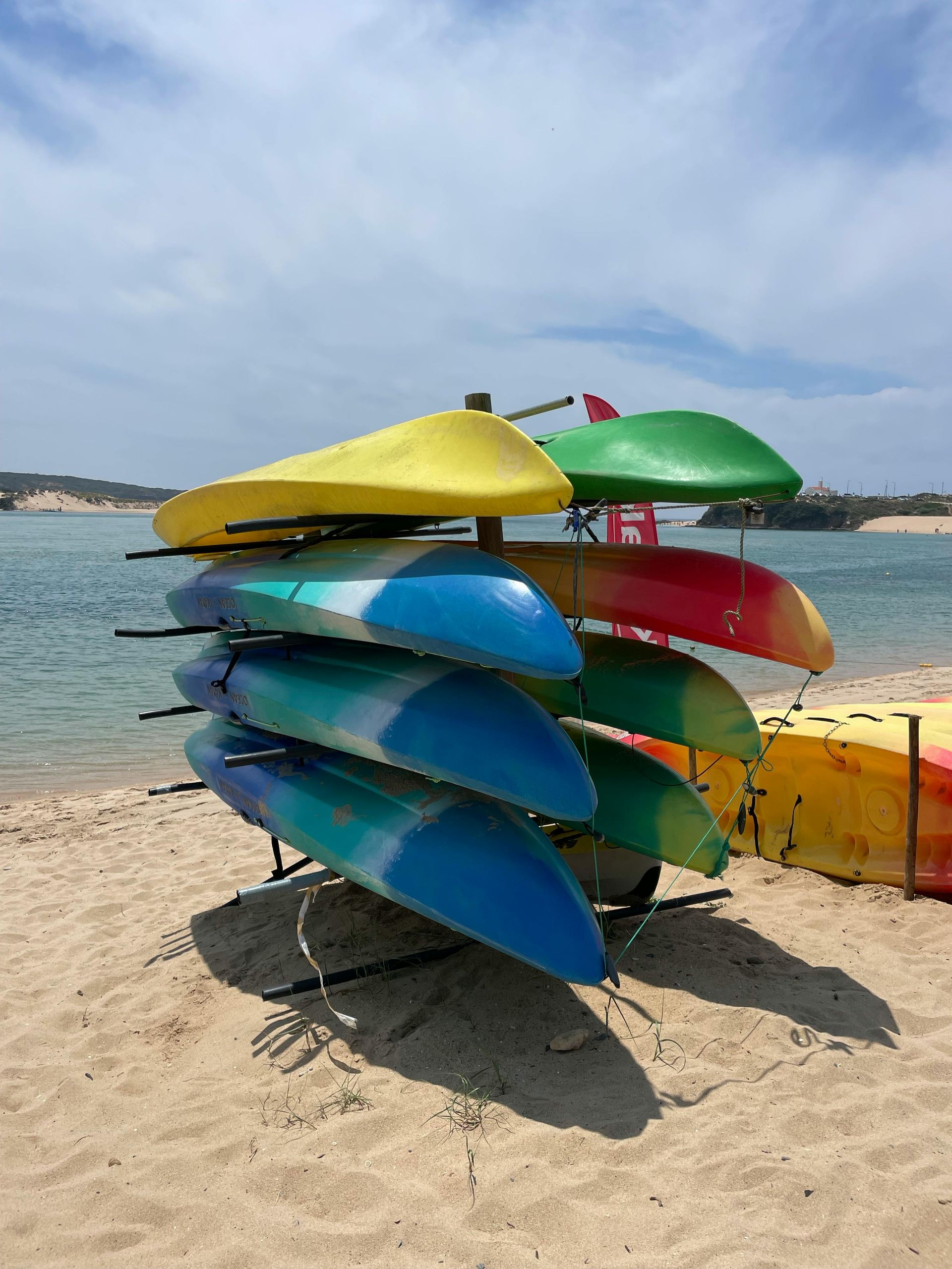 A bunch of kayaks are stacked on top of each other on the beach