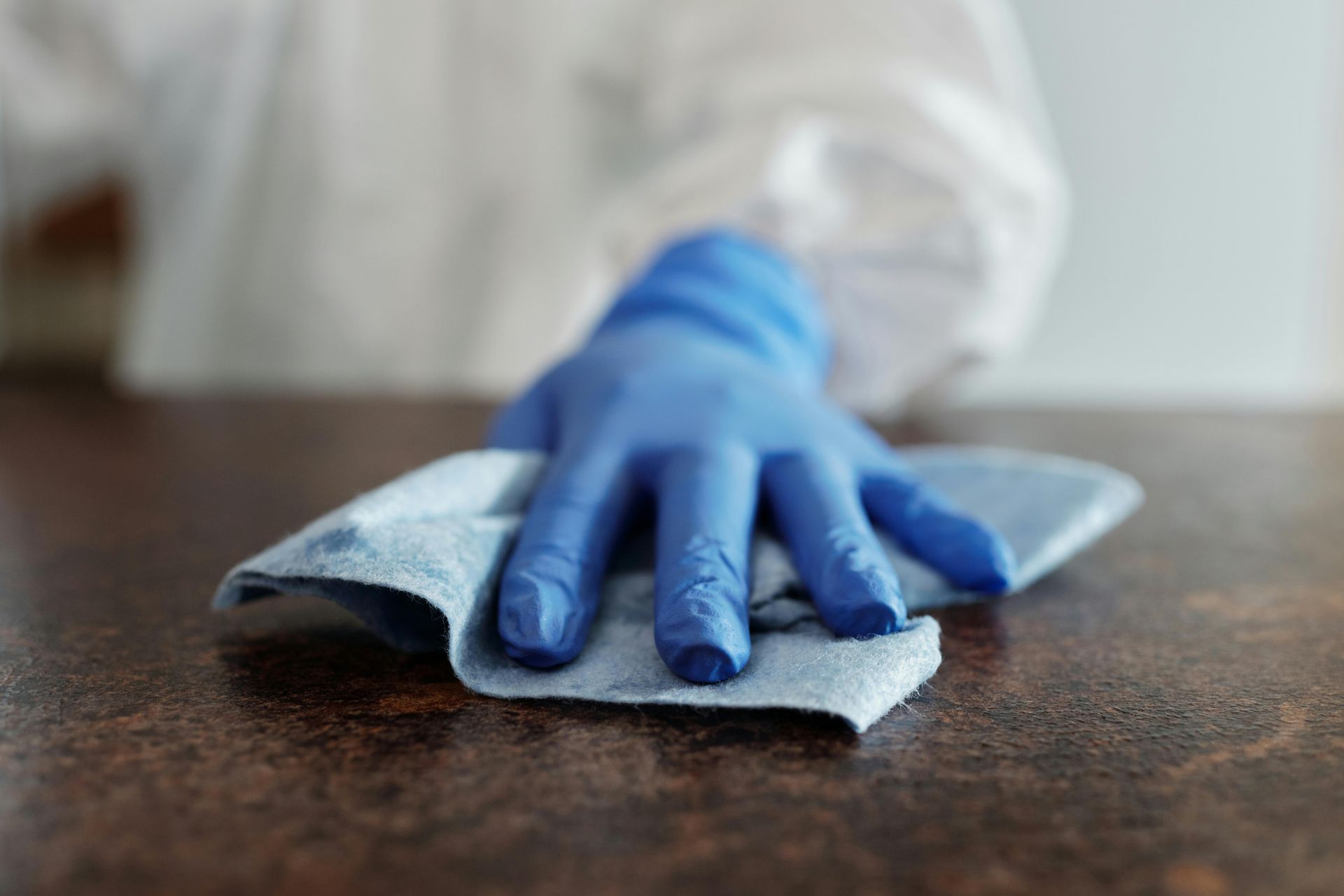 Blue-gloved hand wiping a brown countertop with a blue cloth.