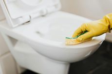 Person in yellow gloves cleans a white toilet with a sponge.