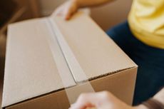 Person holding a closed cardboard box, hands visible. The box is sealed with tape.