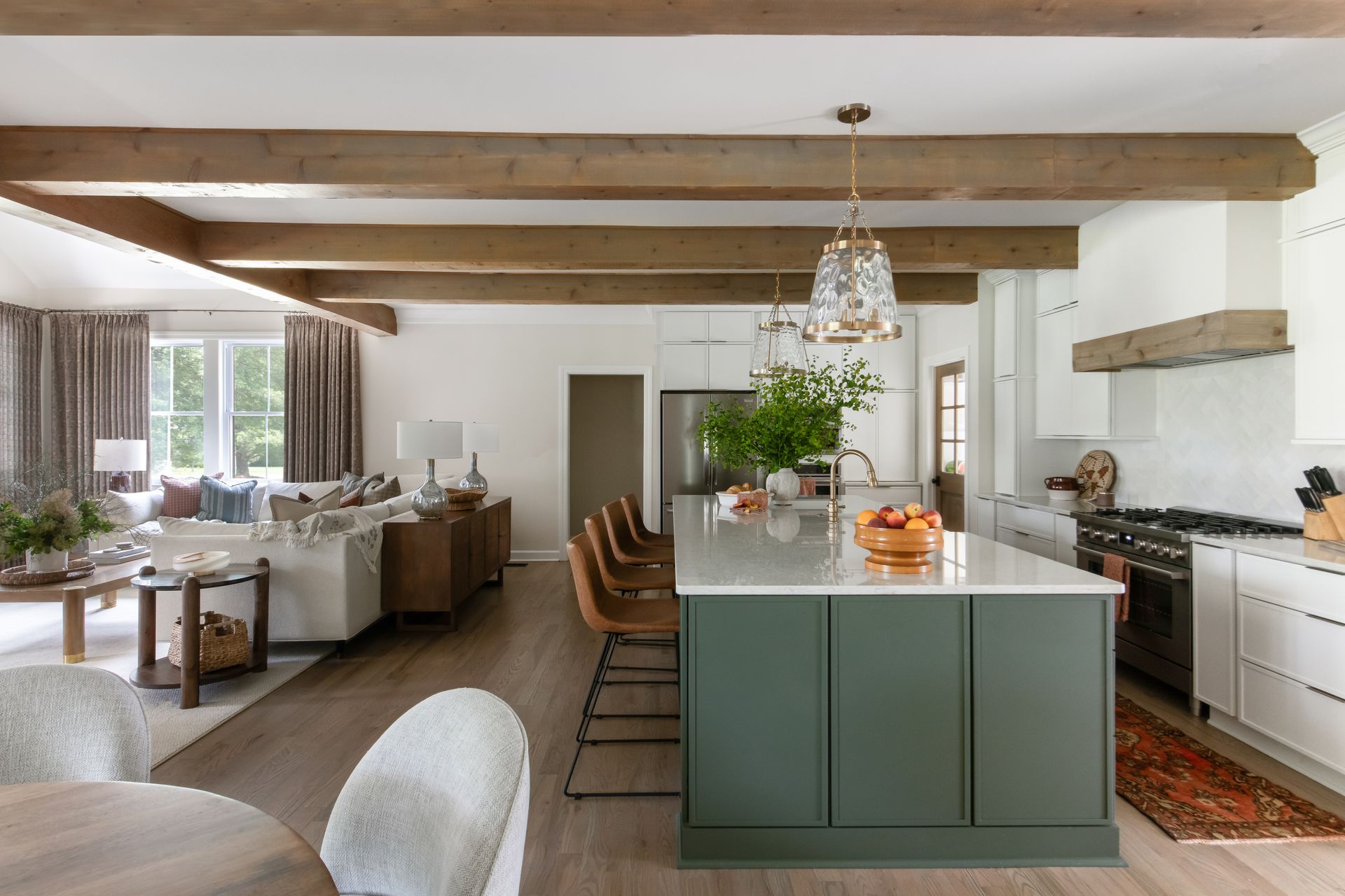 Open-concept kitchen and living area with wooden beams, green island, and white cabinets.