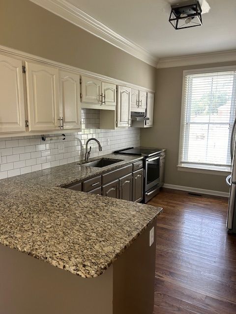 A kitchen with white cabinets, granite countertops, stainless steel appliances, and dark wood floors.