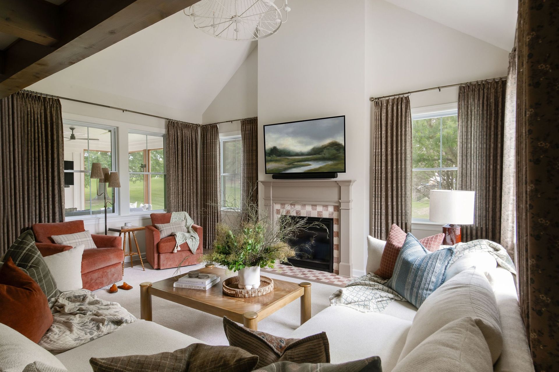 Cozy living room with white sofa, fireplace, red armchairs, and brown curtains.