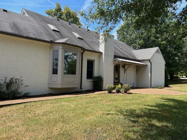 White brick house with a bay window, chimney, and front porch on a grassy lawn.