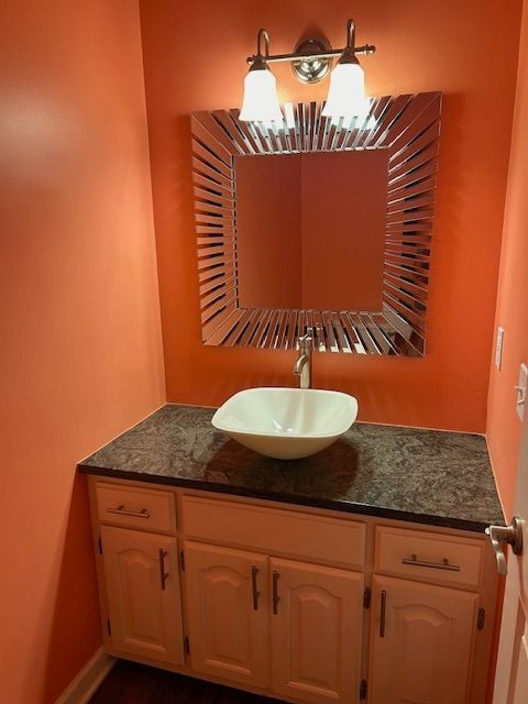 Bathroom with peach walls, white vanity, dark countertop, decorative mirror, and vessel sink.