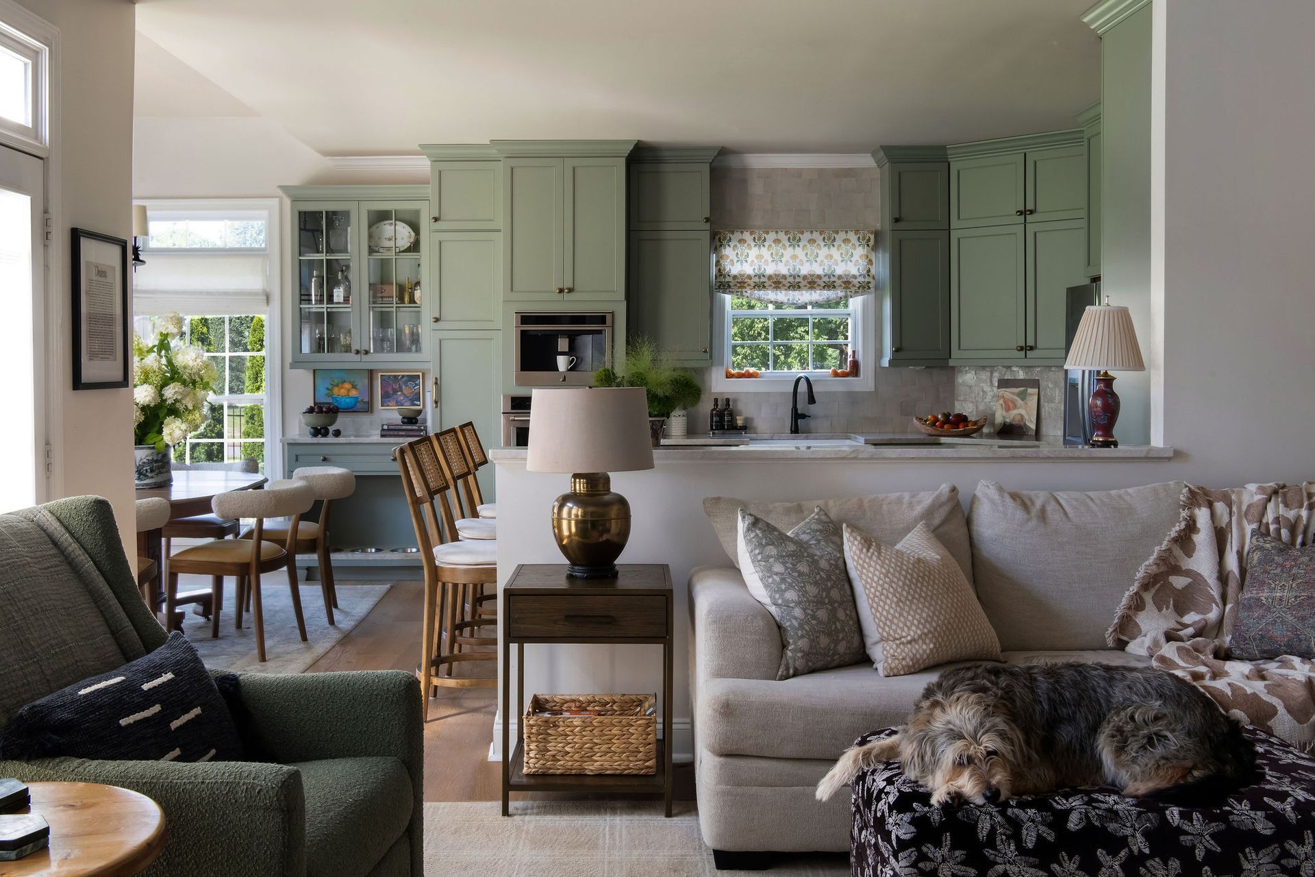Open concept kitchen and living area with green cabinets, sofas, and a cat.