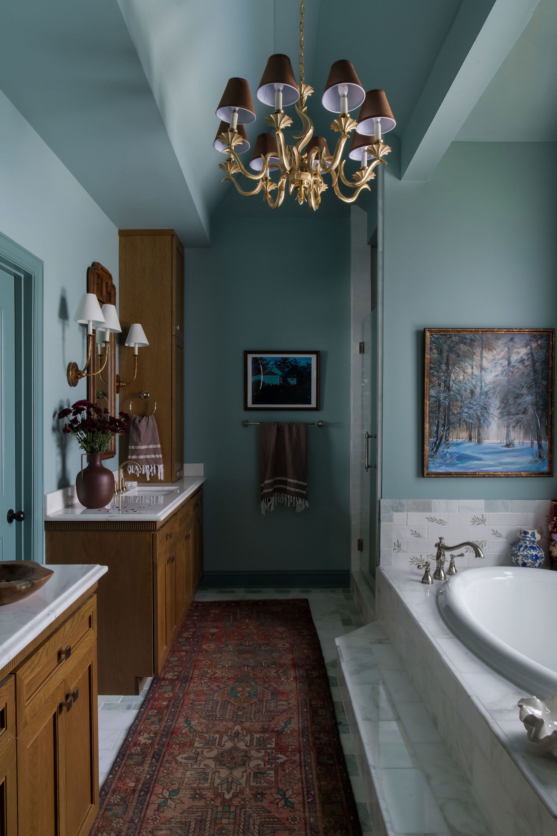 Bathroom with a teal-colored ceiling and walls, wooden cabinets, a Persian rug, and a golden chandelier.