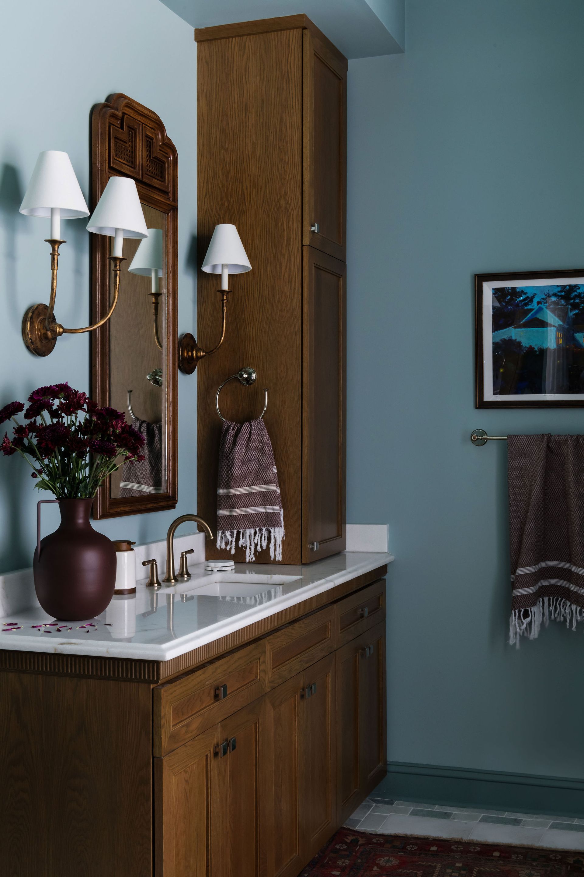 Bathroom with wooden vanity, tall cabinet, teal walls, and decorative accents.