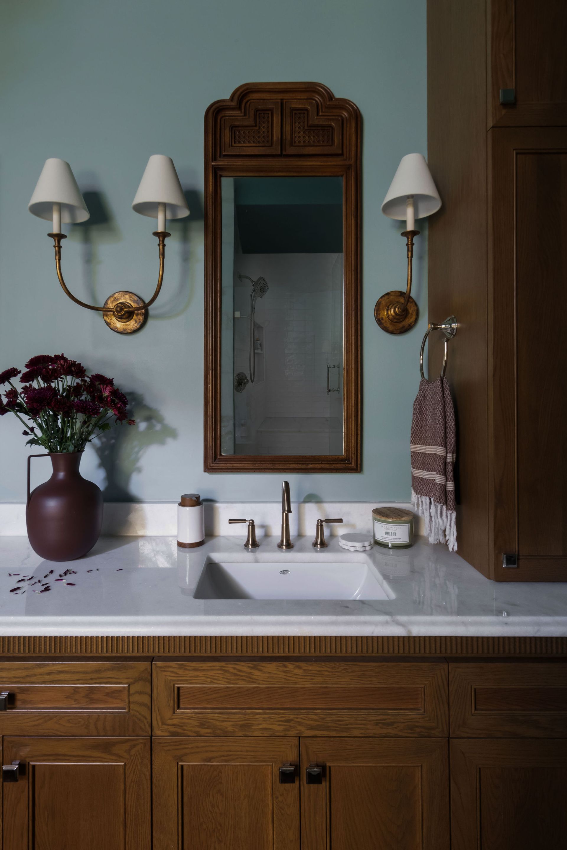 Bathroom with a wooden vanity, marble countertop, mirror, sconces, and blue walls.