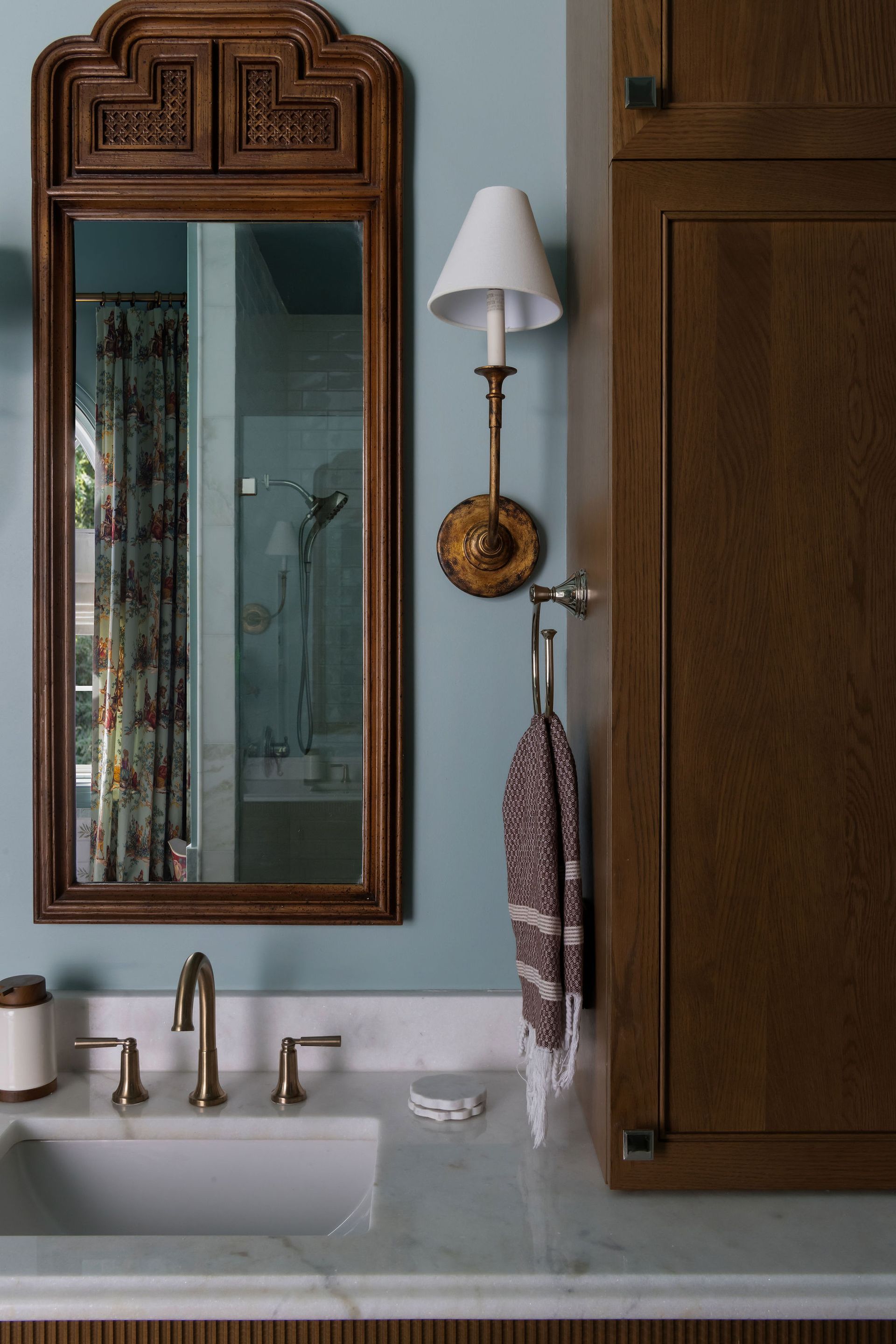 Bathroom with blue walls, a wooden mirror, sconce, sink, and wood cabinet.