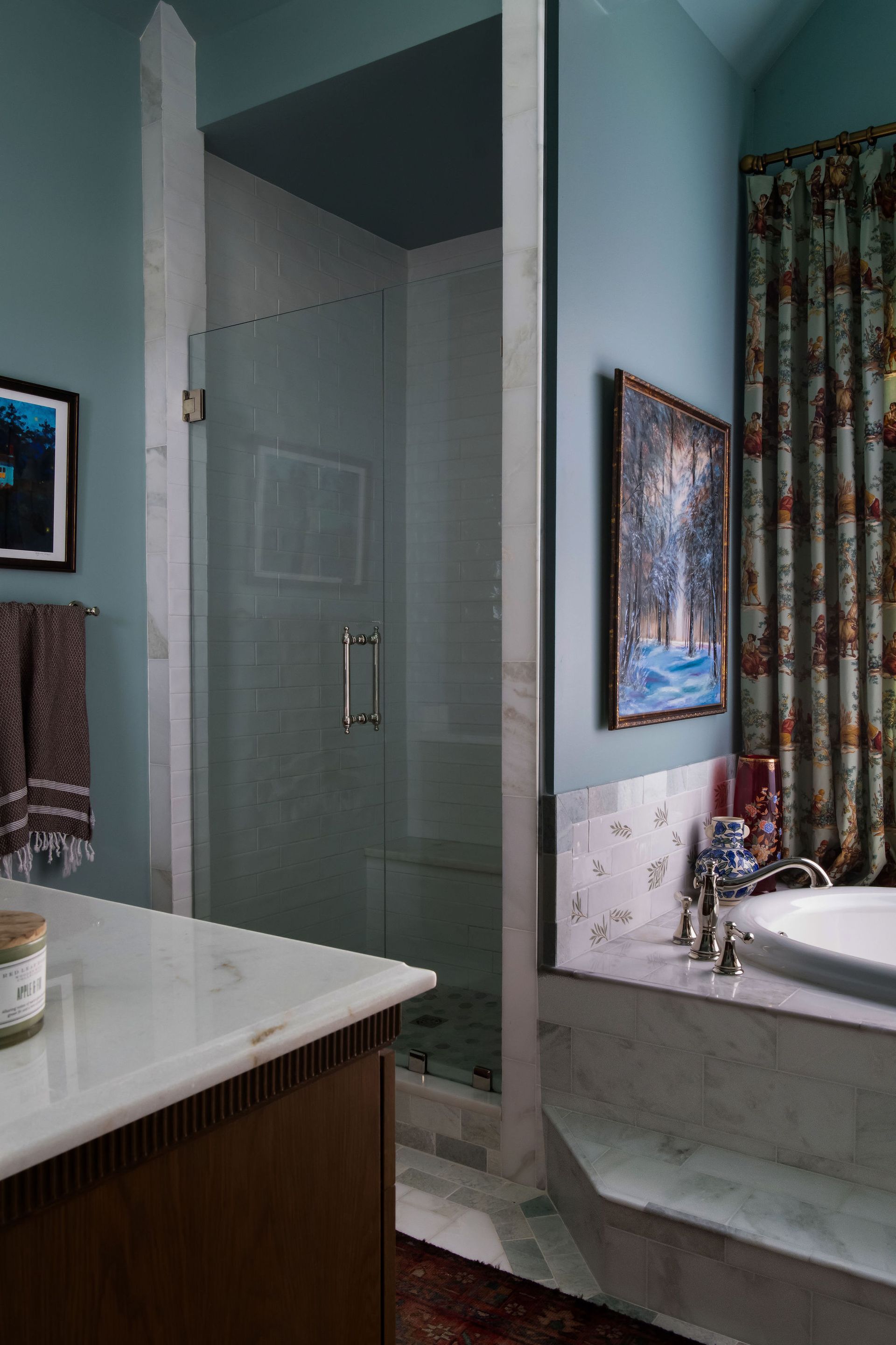 Bathroom with shower, tub, and vanity; light blue walls, marble accents, and artwork.