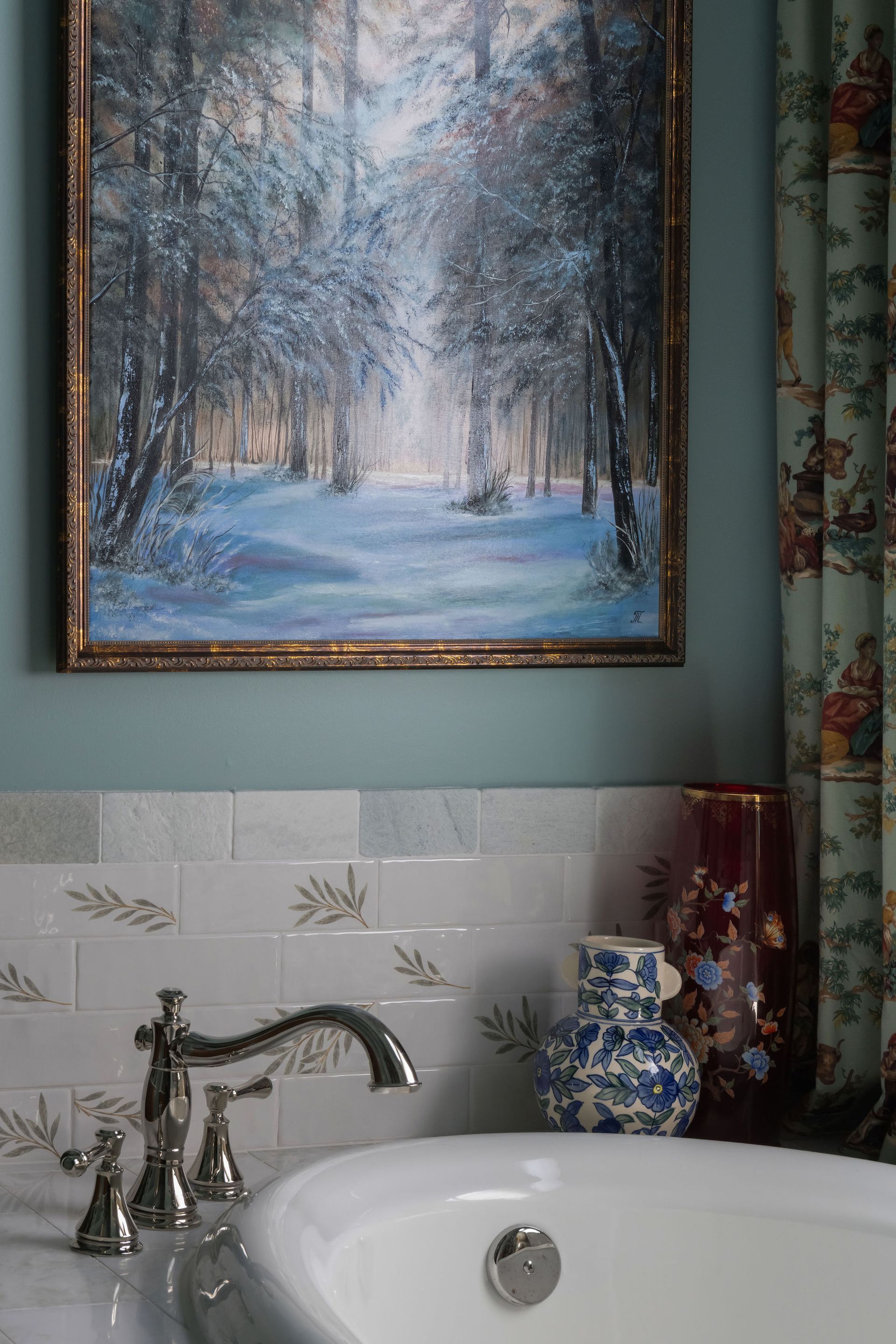 Bathroom with a framed forest painting above a white tub and decorative vases.