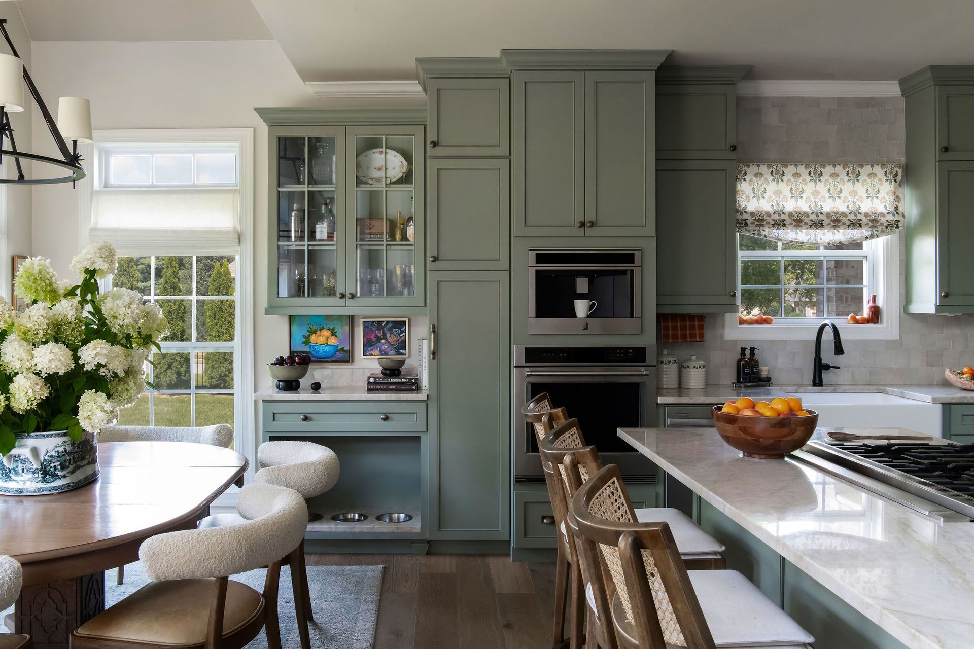 Sage green kitchen with white countertops, wood stools, and a dining table with chairs.