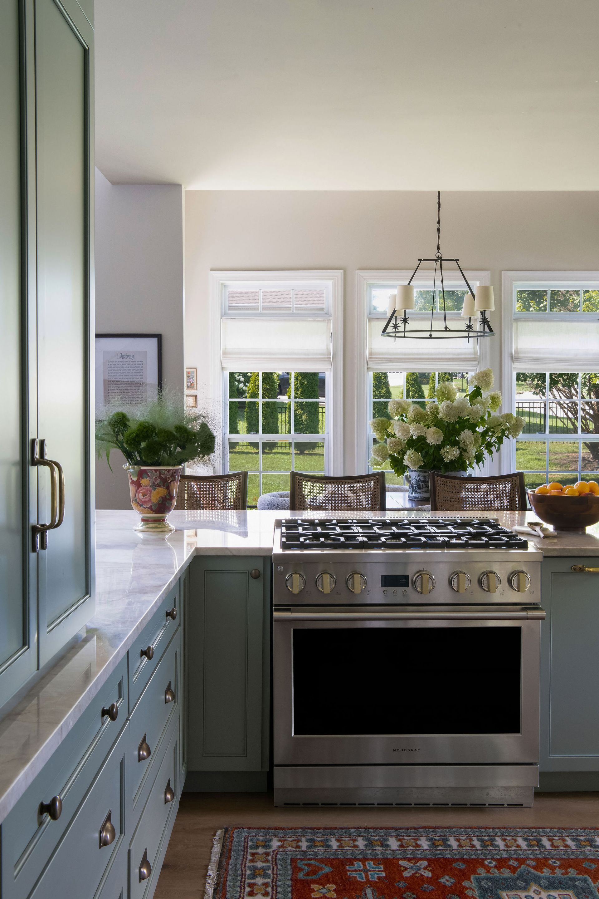 Blue kitchen with stainless steel stove, marble countertop, windows, and a patterned rug.