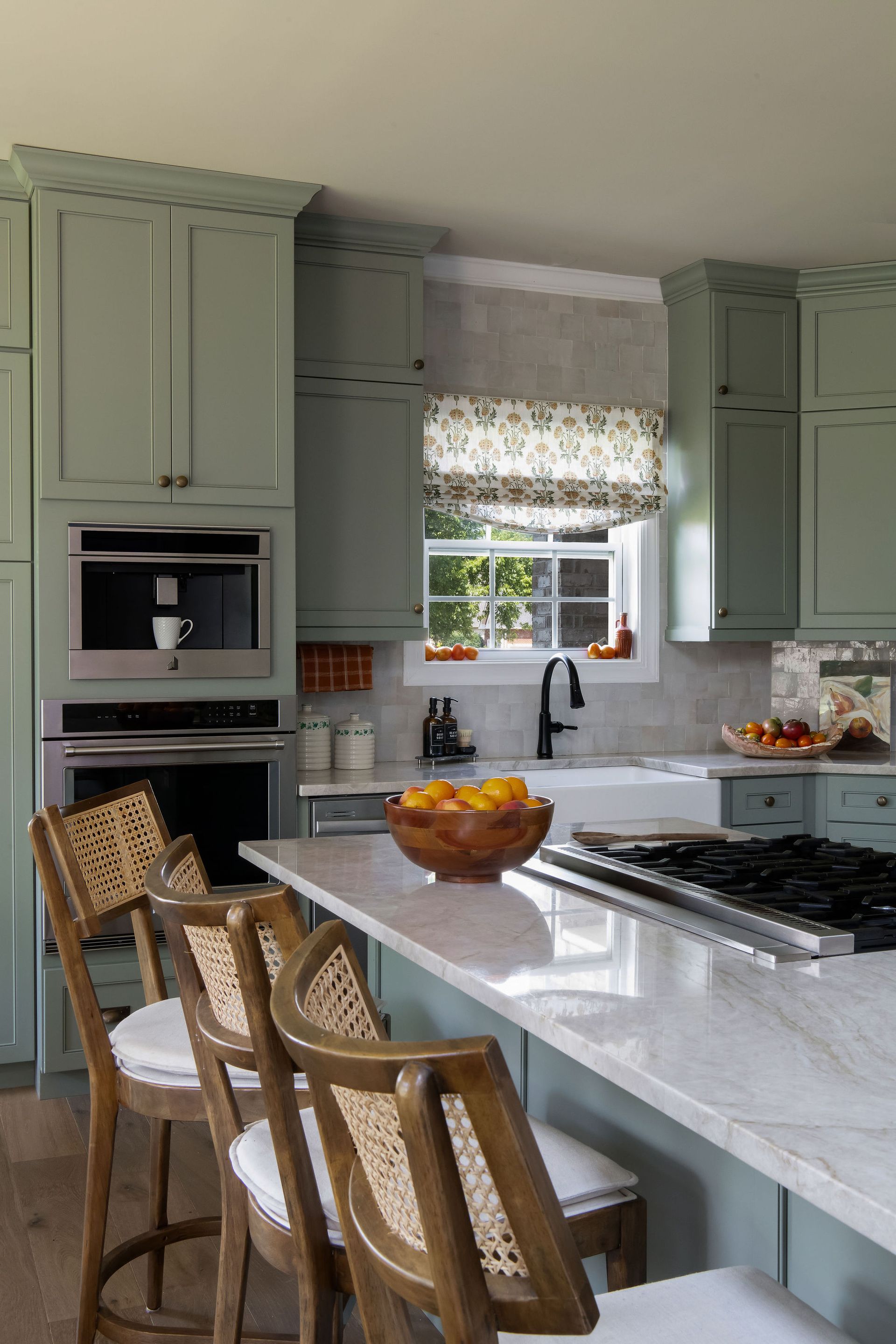 Sage green kitchen with island, bar stools, and a window with a patterned shade.