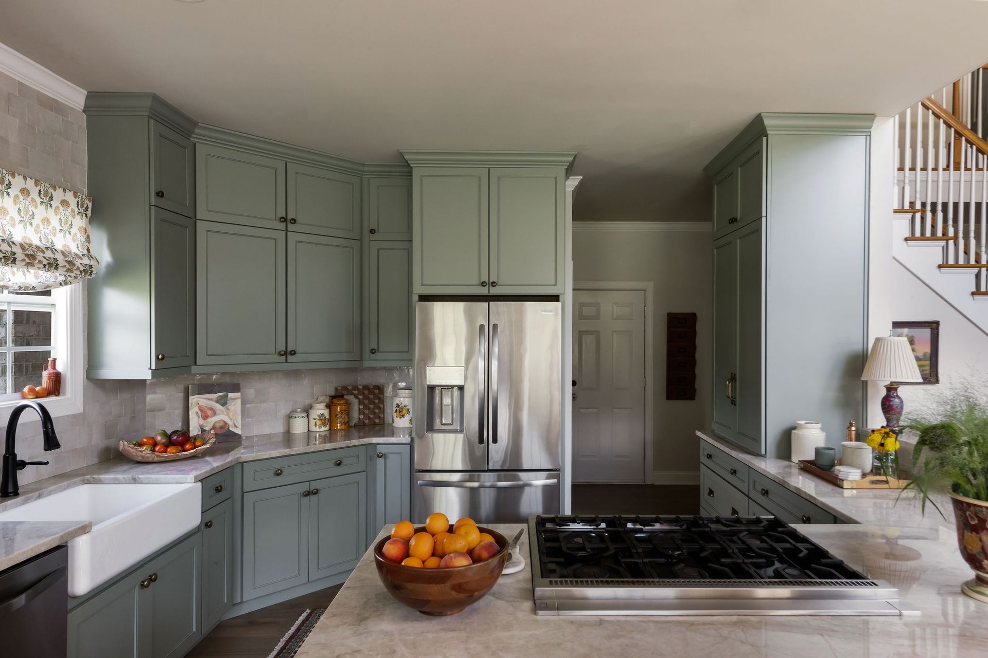 Green kitchen with stainless steel appliances and fruit bowl.