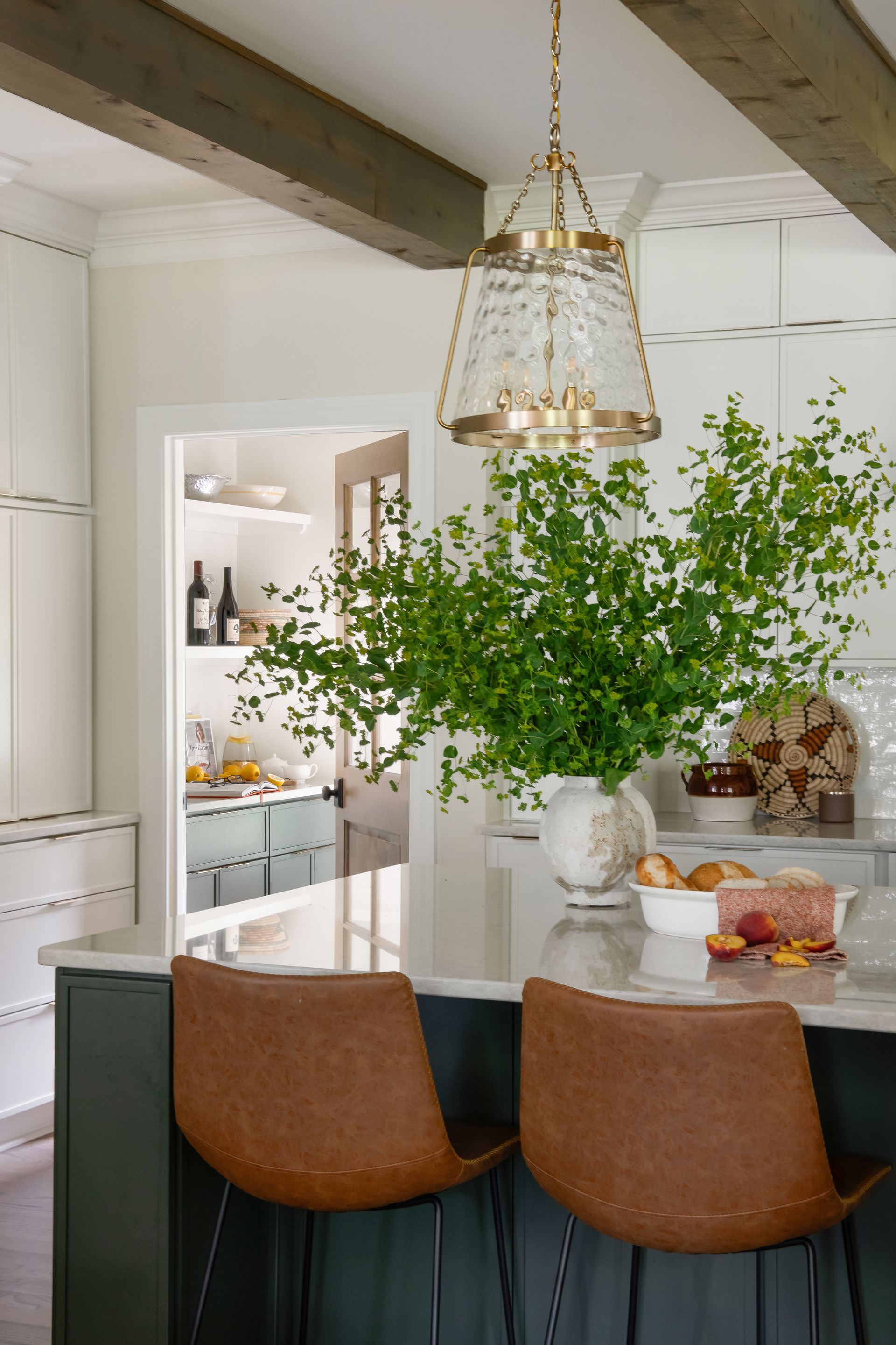 Kitchen with green island and brown leather bar stools, illuminated by a glass pendant.