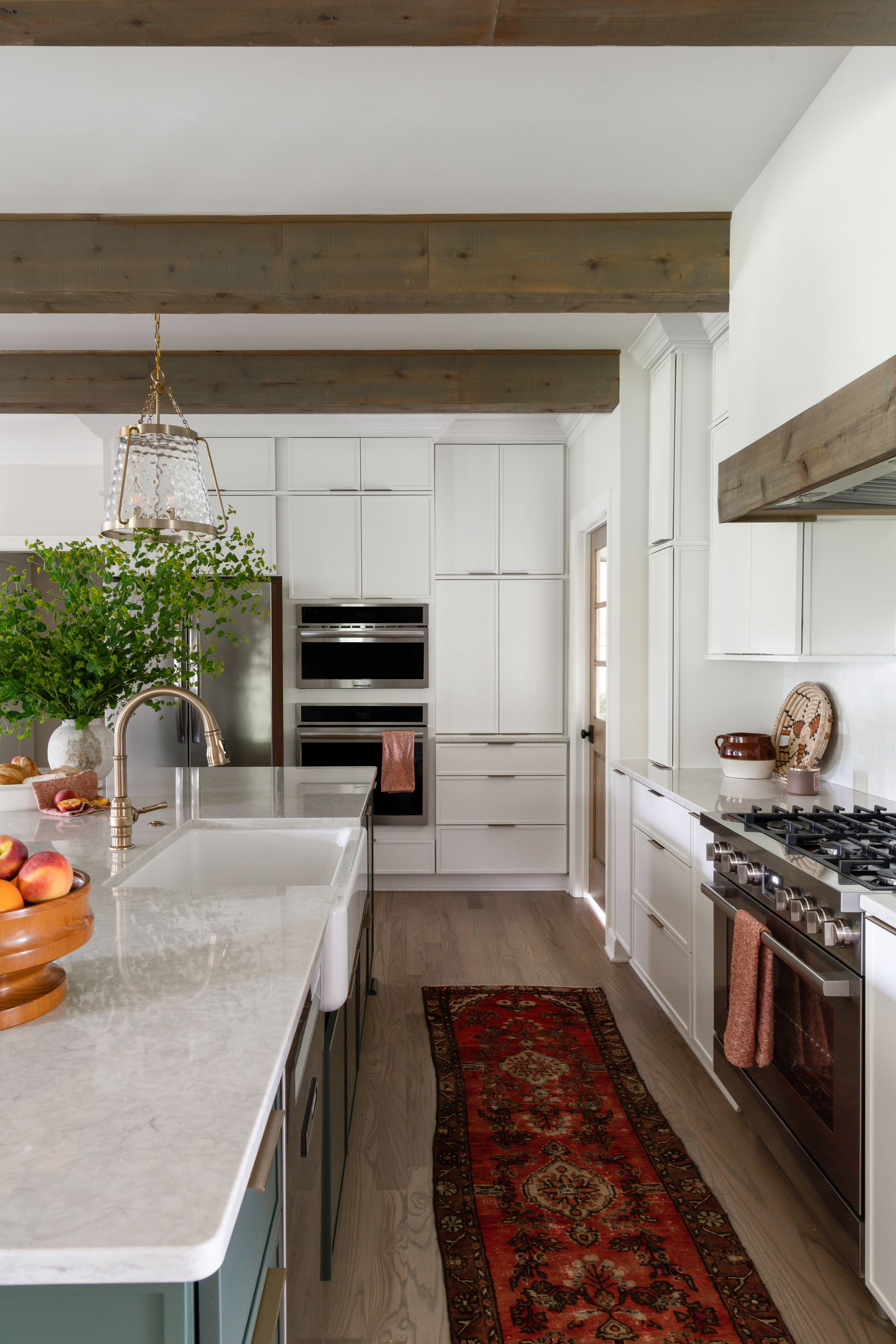 Kitchen with white cabinets, wood beams, marble countertops, and a colorful runner.