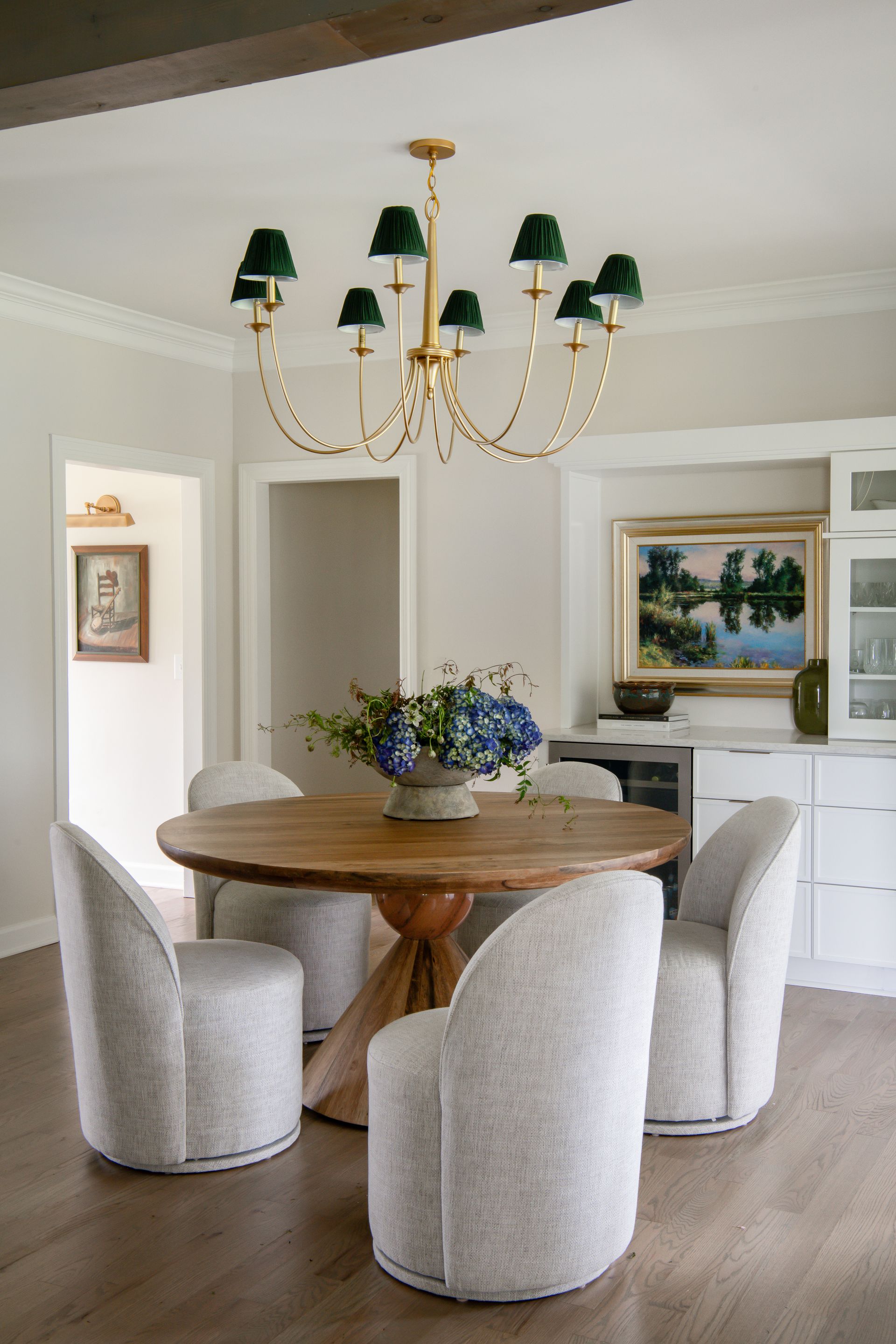 A dining room with a round wooden table, white chairs, and a gold chandelier with green shades.
