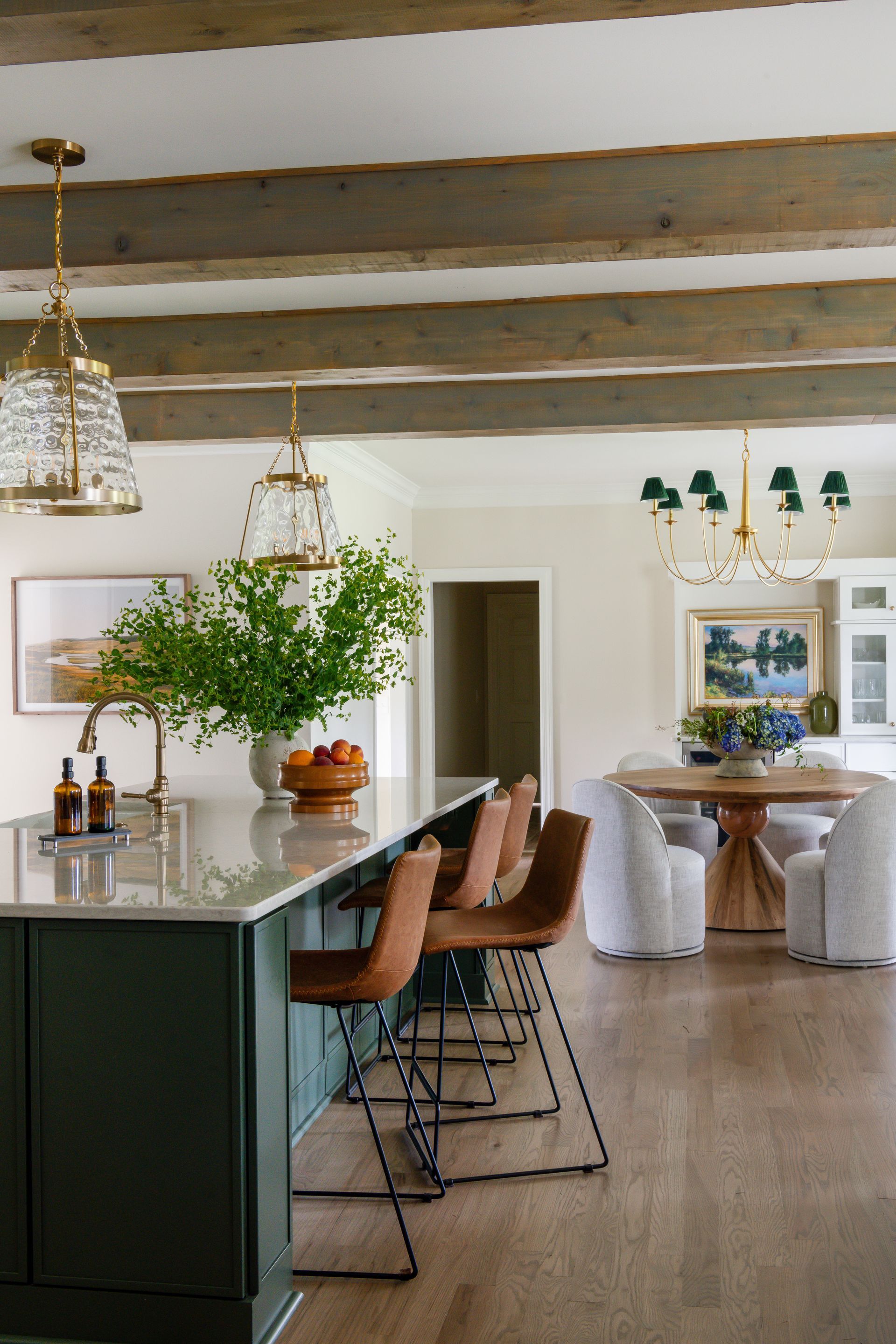 Kitchen with green island, wooden beams, brown bar stools, and dining area with round table.