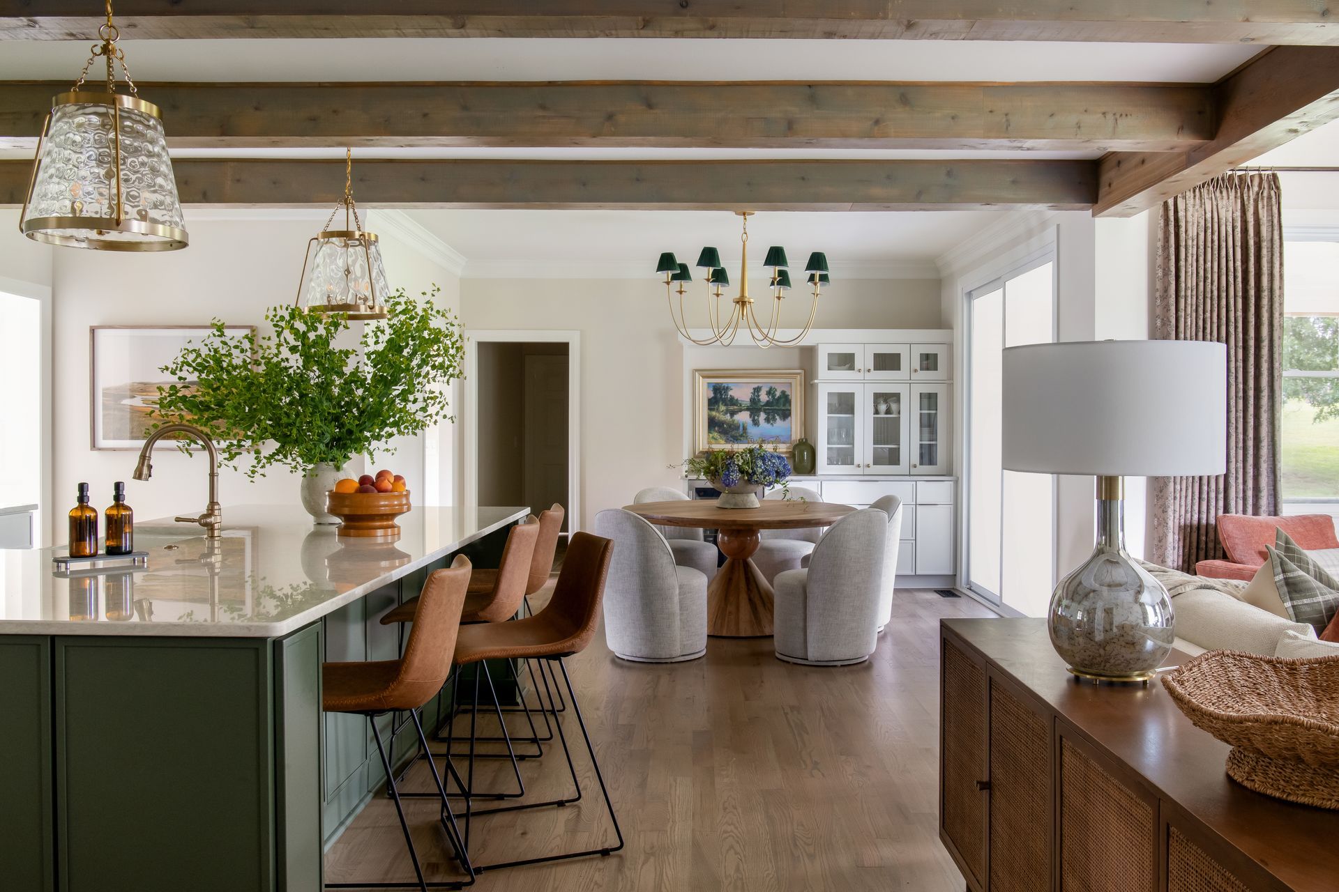 Open-concept kitchen and dining area with sage green island, wood beams, and dining table.