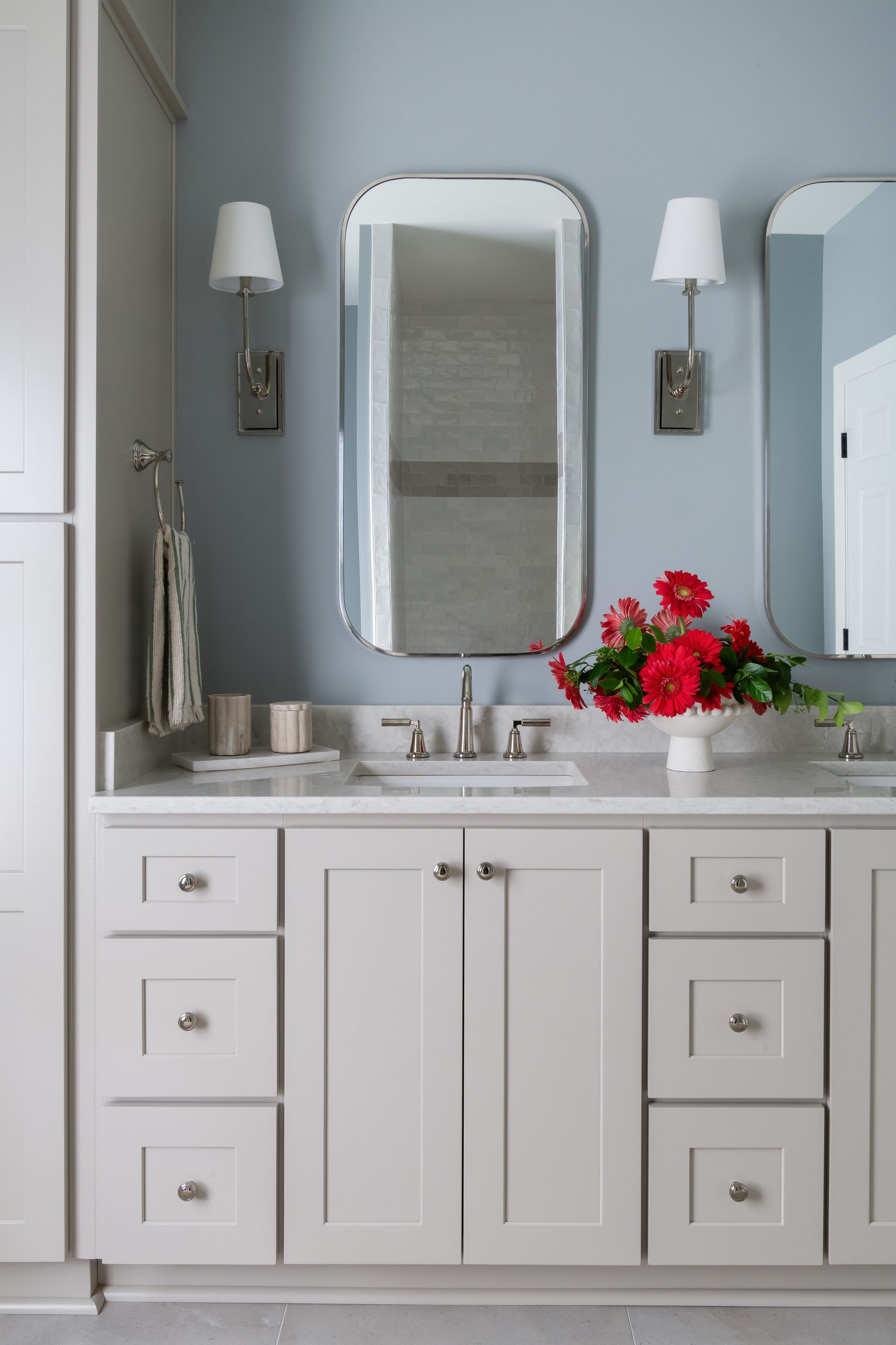 Bathroom vanity with two mirrors, white cabinets, blue walls, and red flowers.