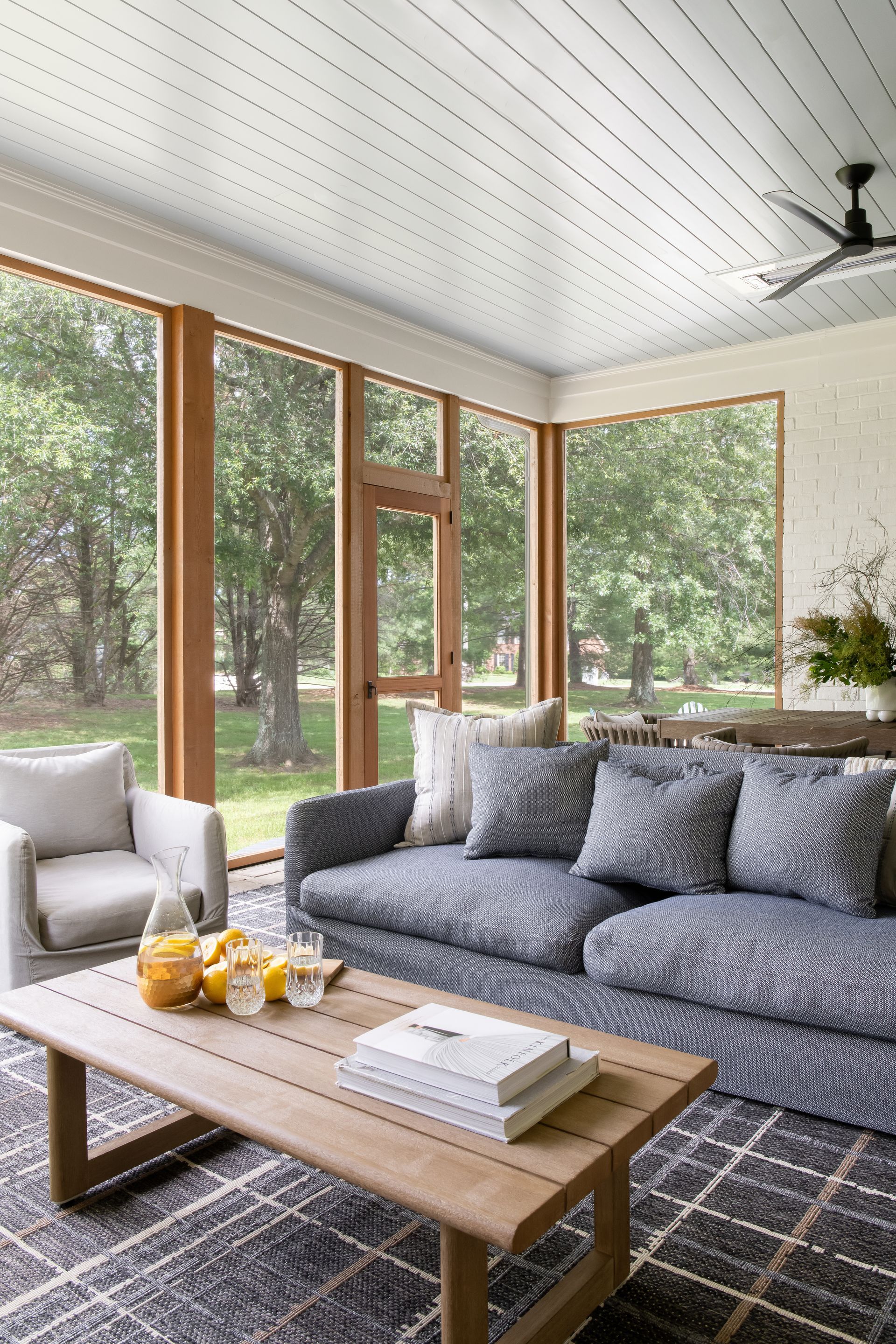 Screened porch with blue sofa, wooden coffee table, and view of trees.