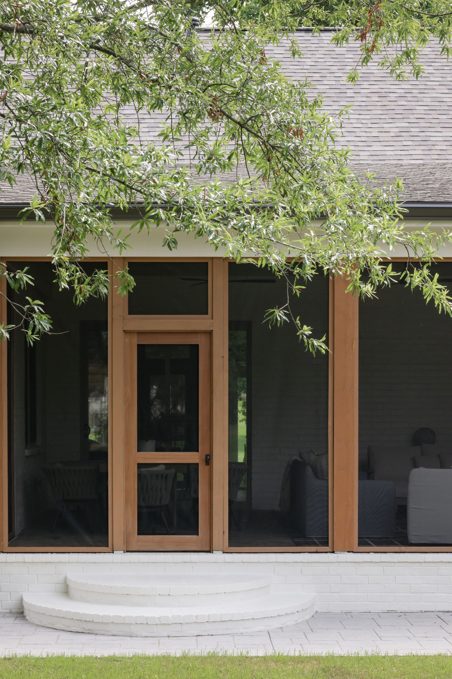 Screened porch entrance with wooden door and pillars, white steps, and overhanging tree branches.