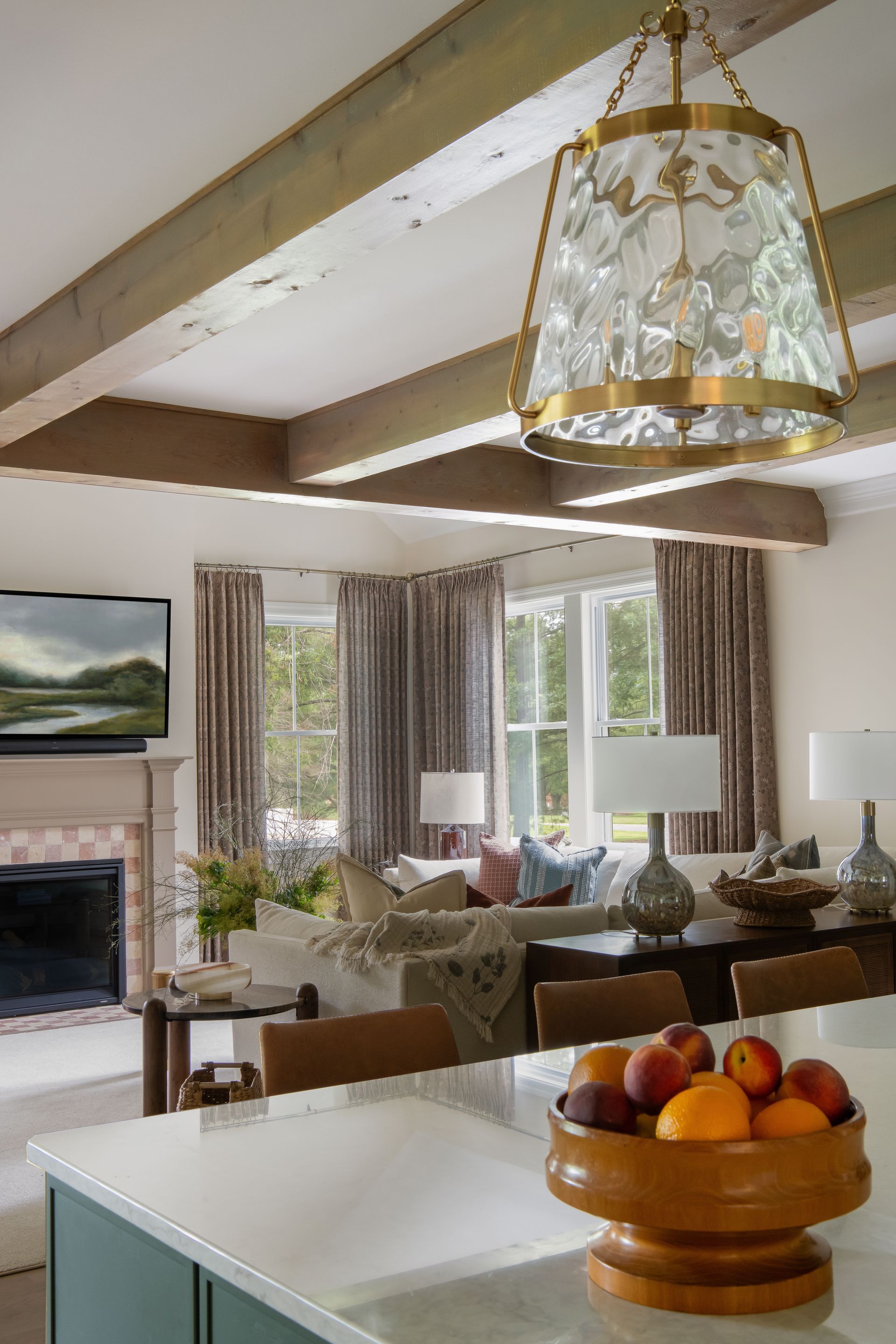 Living room with a crystal chandelier, wooden beams, fireplace, and a fruit bowl.