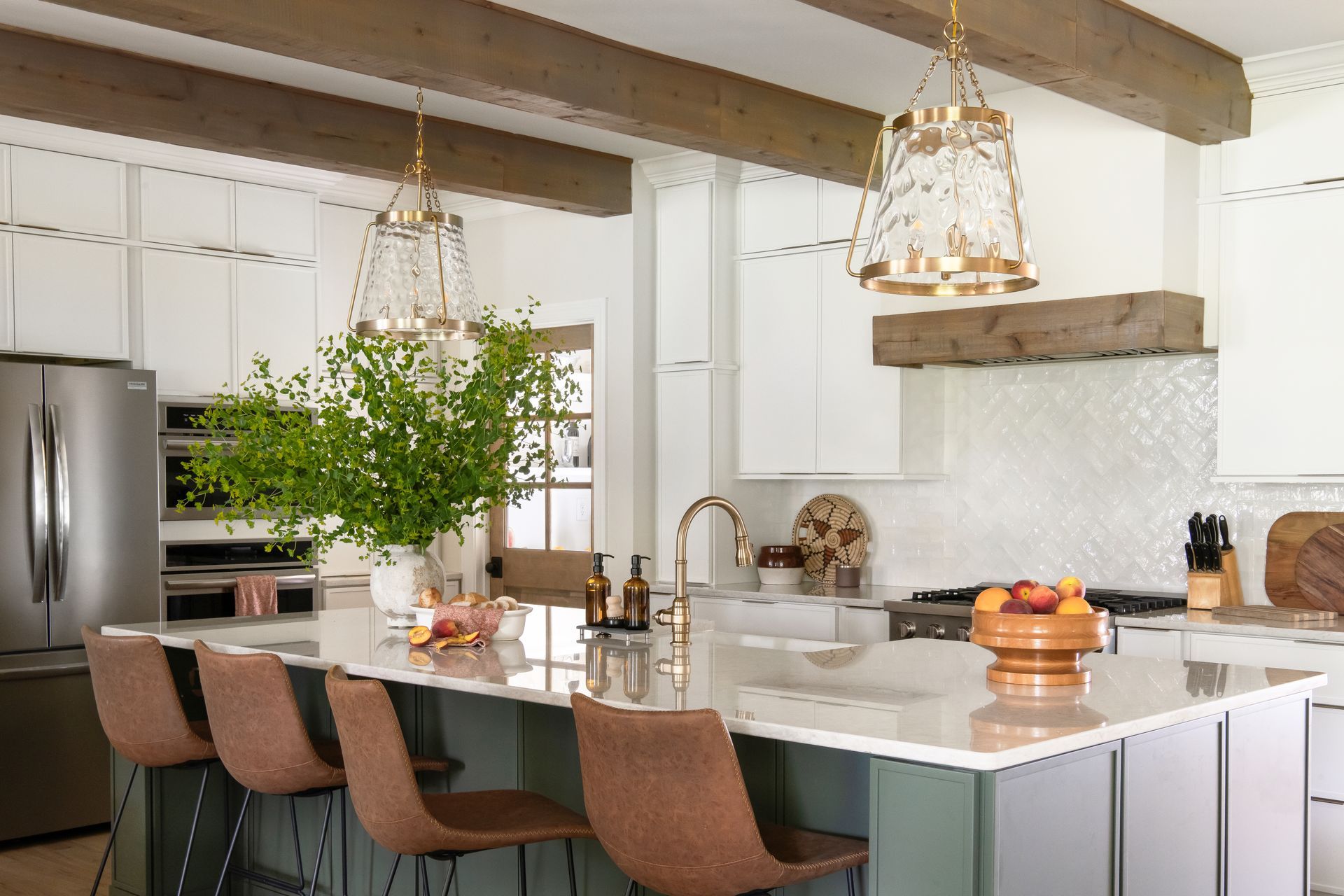 Kitchen with island, green cabinets, brown bar stools, gold fixtures, and wood beams.