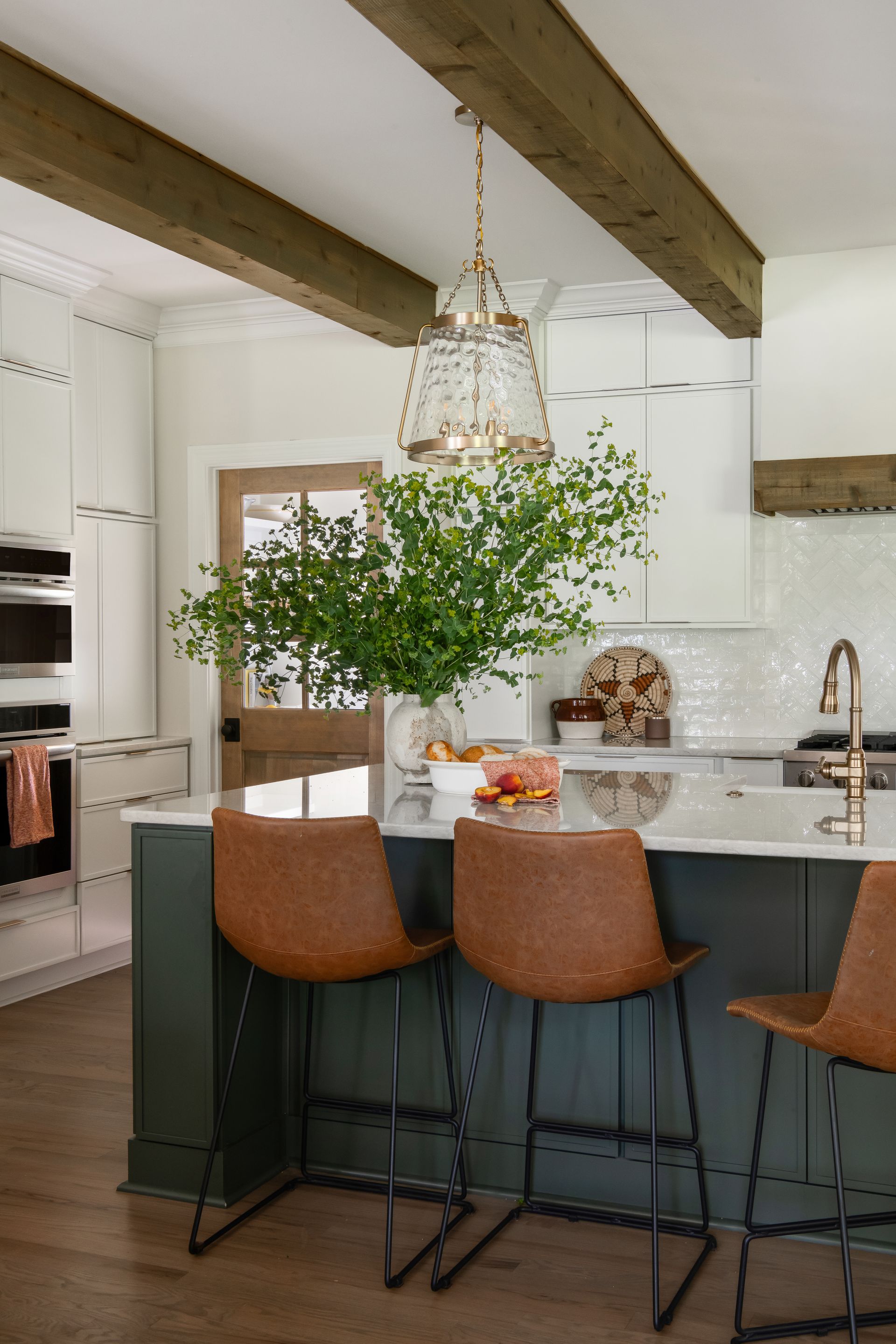 Kitchen with green island, brown leather bar stools, and a pendant light.