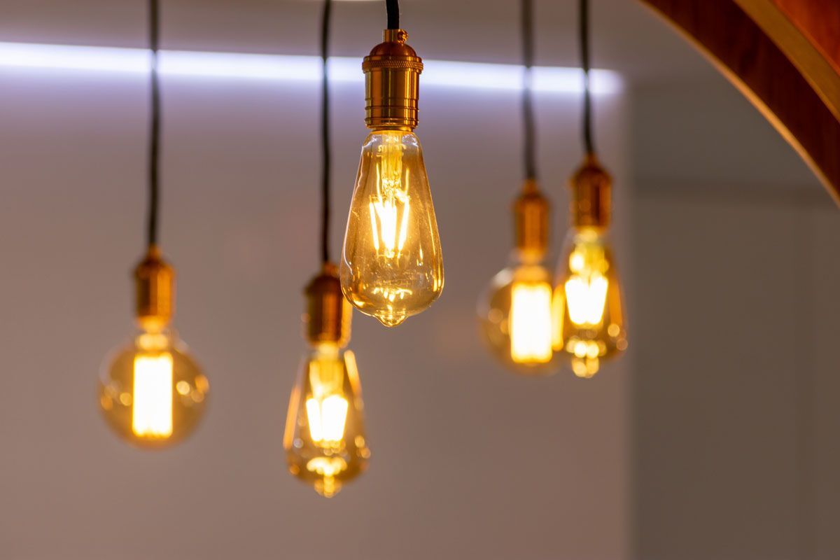 Five glowing Edison-style light bulbs hanging from black cords, amber light, neutral background.