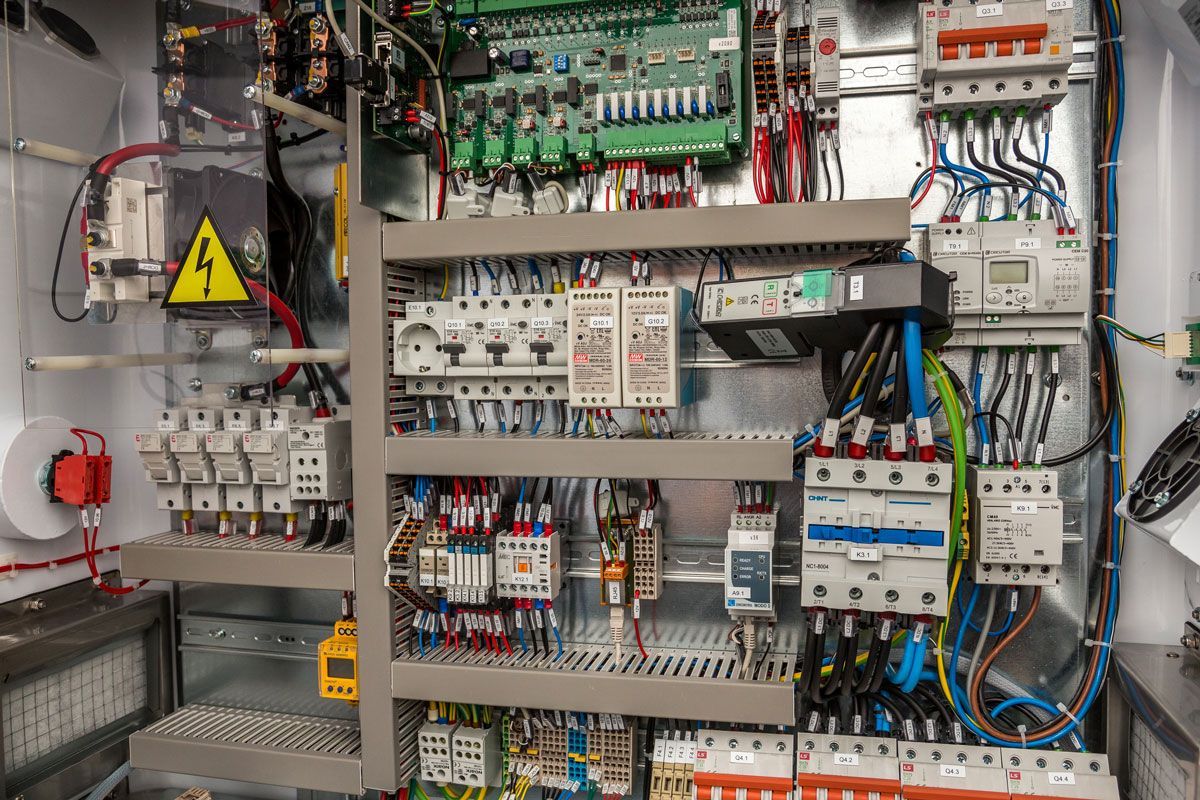Electrical panel with various switches, wires, and circuit breakers. Yellow caution sign present.