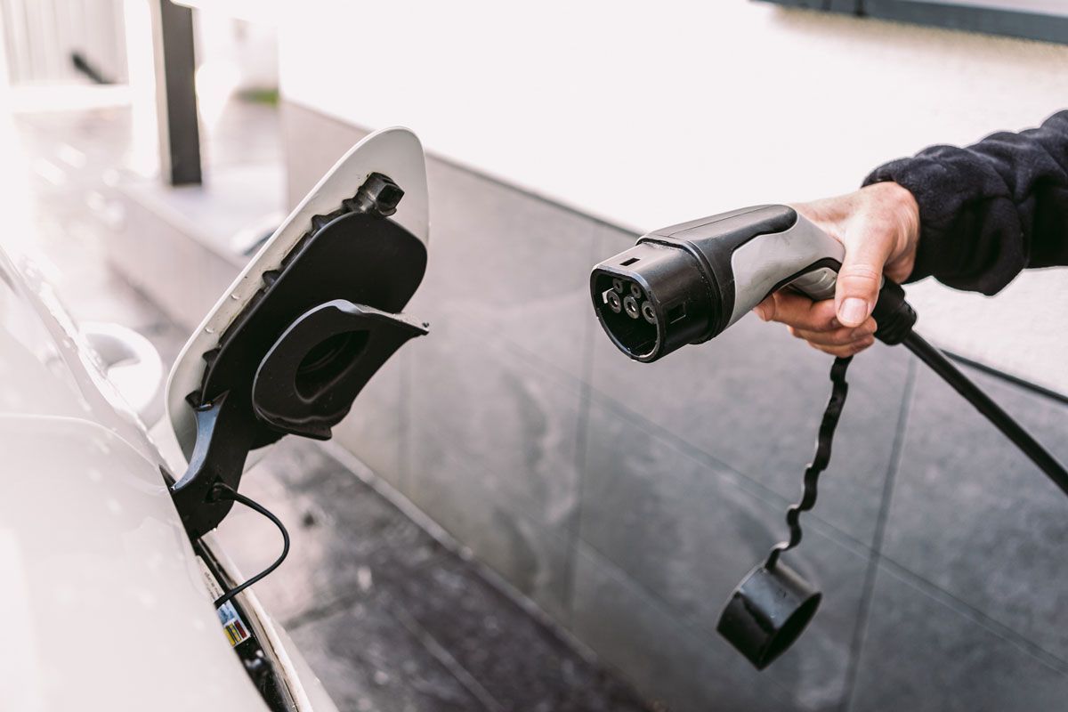 Person plugging an EV charging cable into a white car's charging port.