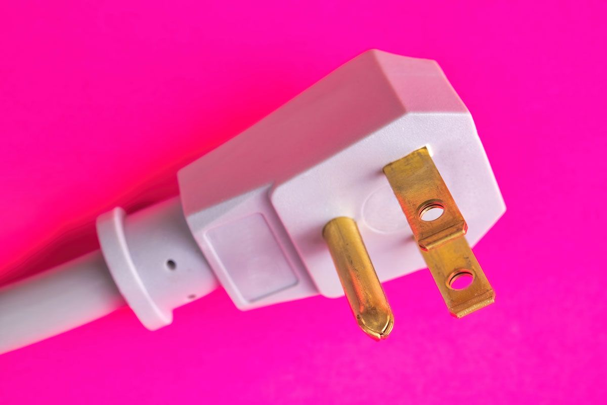 White angled electrical plug with three prongs on a pink background.