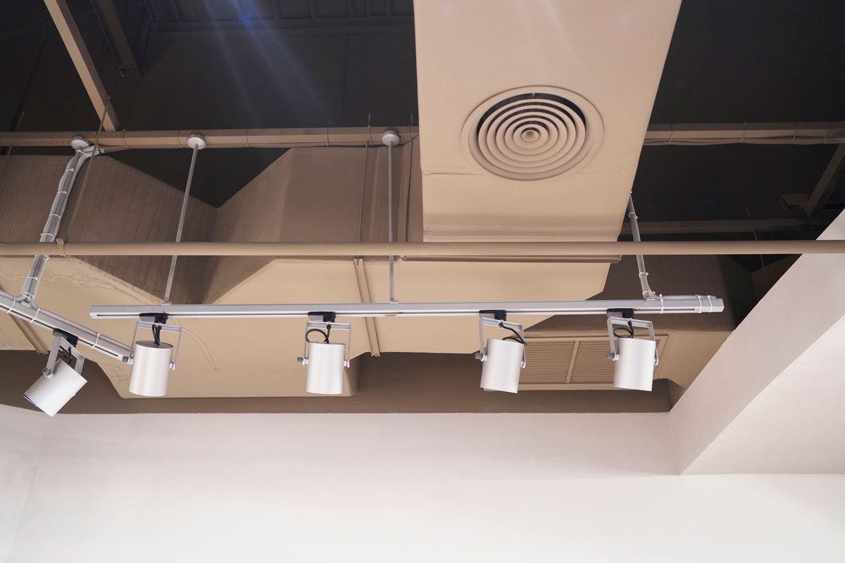 A row of four white spotlights hangs from a track on a tan ceiling. Ductwork and air vent are visible.