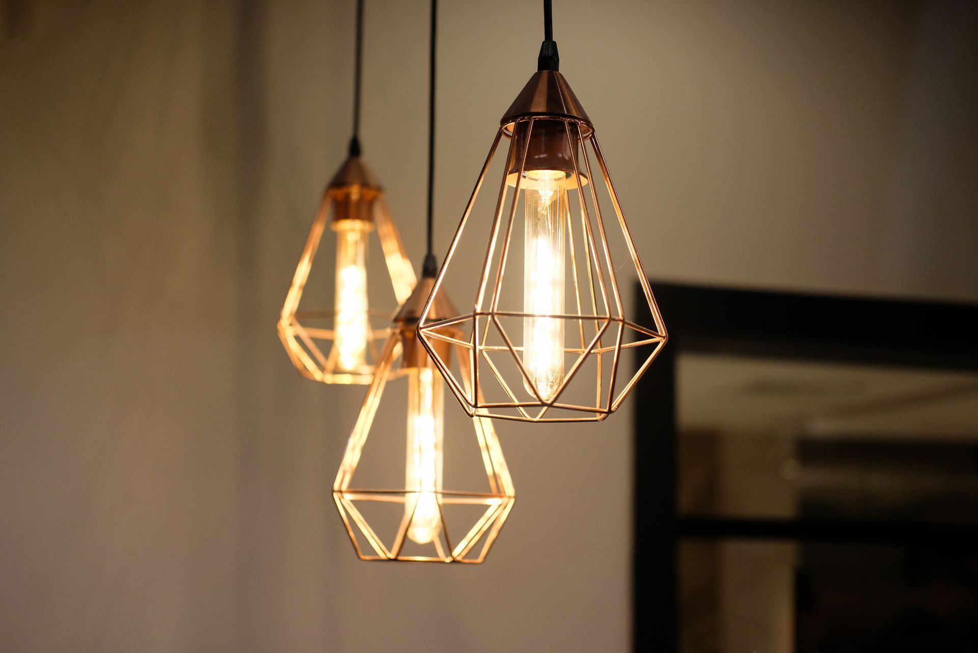 Three pendant lights with copper diamond-shaped cages, lit with warm Edison bulbs.