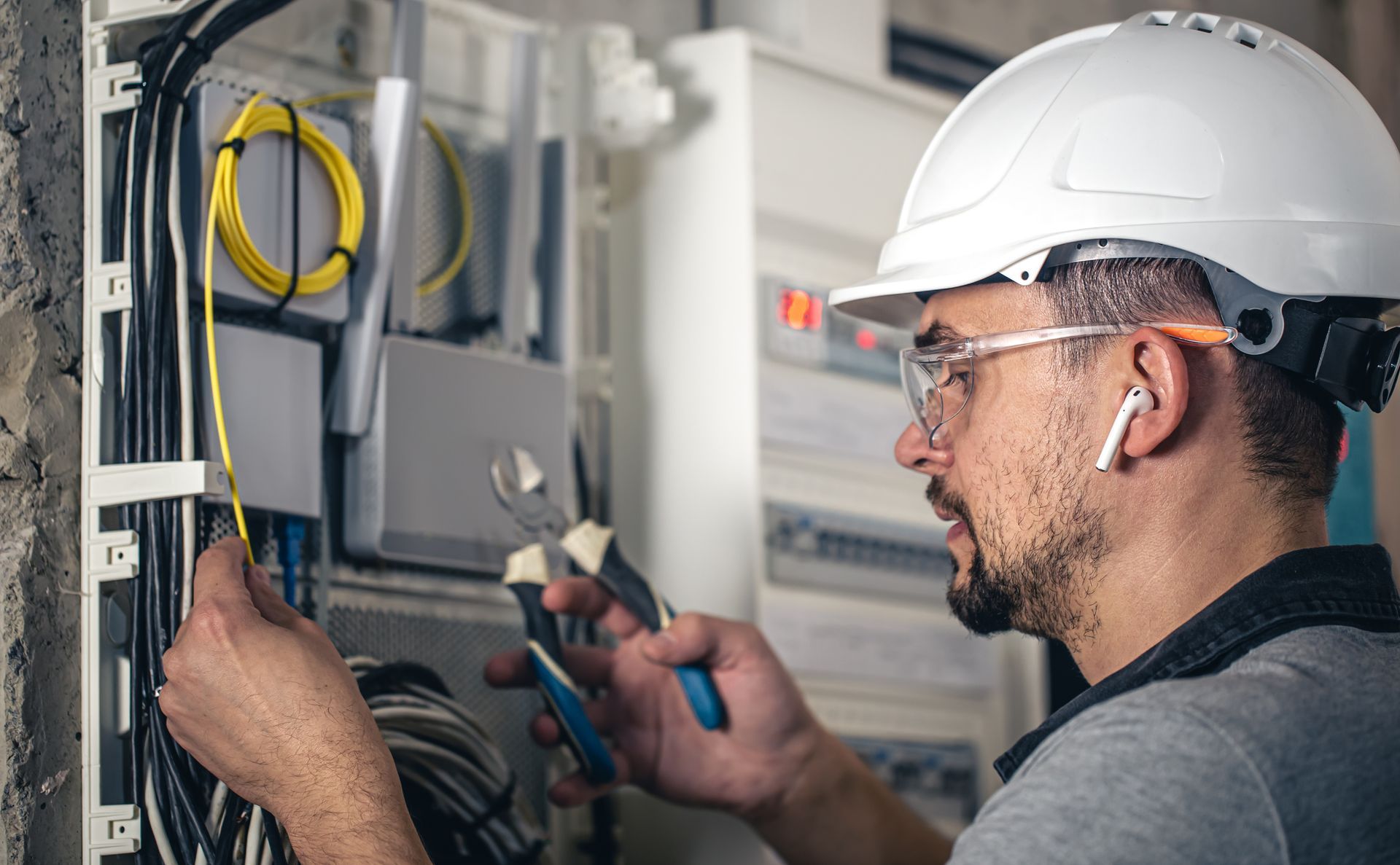 Electrician in a hard hat and safety glasses working on wiring in a control panel.