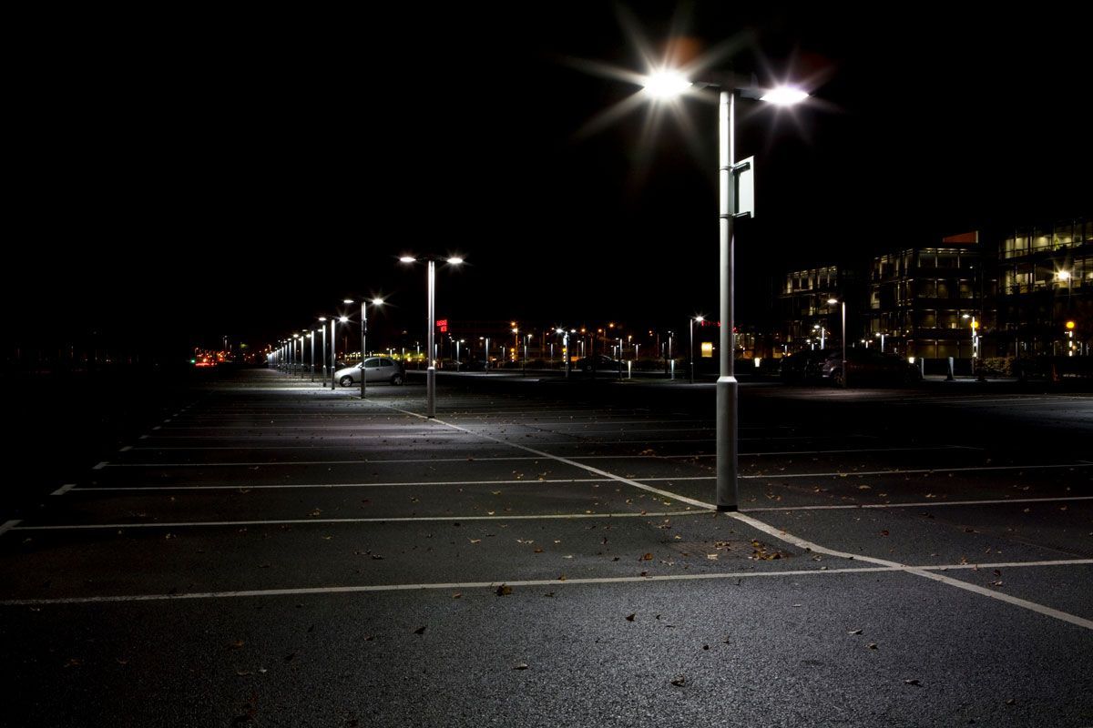 Empty, dark parking lot at night, illuminated by streetlights, with a distant building in the background.