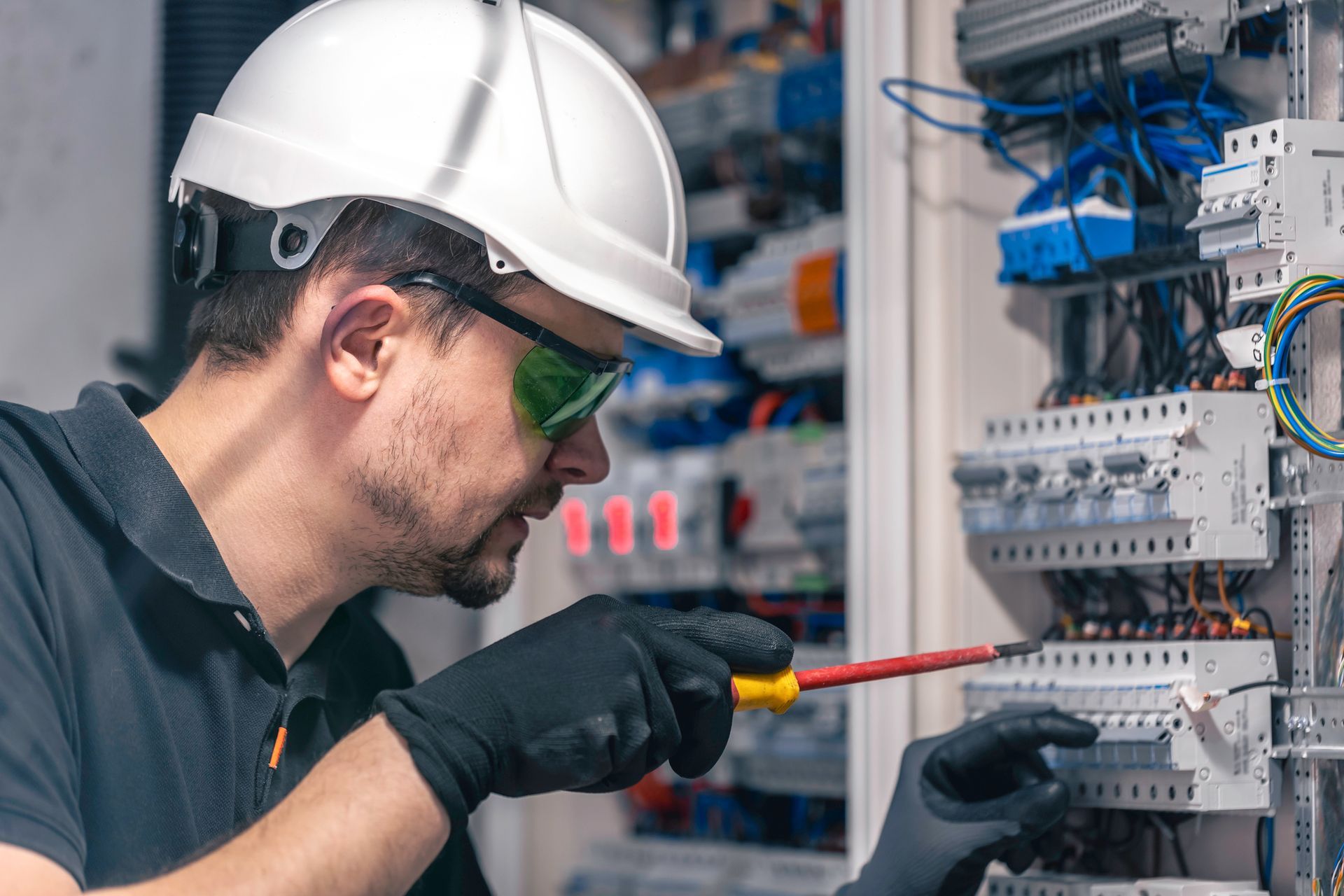 Electrician with gloves and safety glasses working on electrical panel.