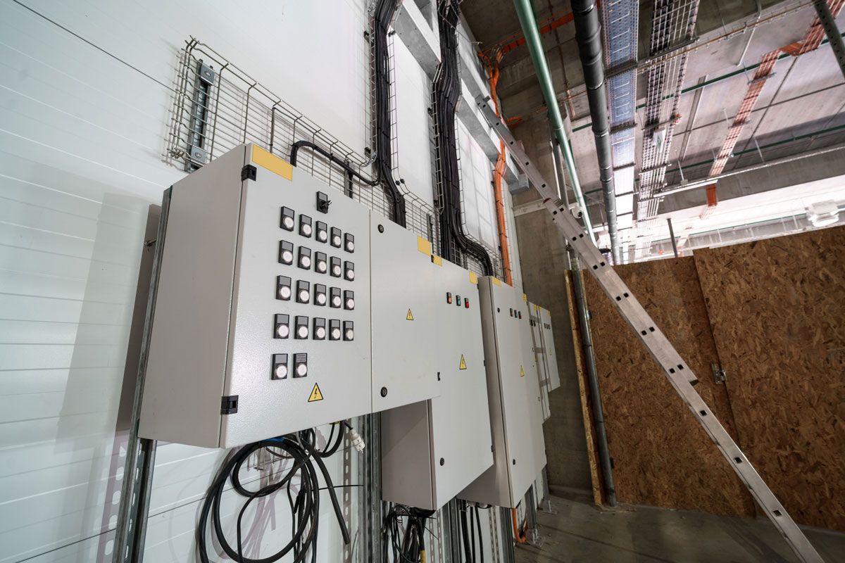 Electrical control panels mounted on a white wall in a construction site, with conduits and wires.