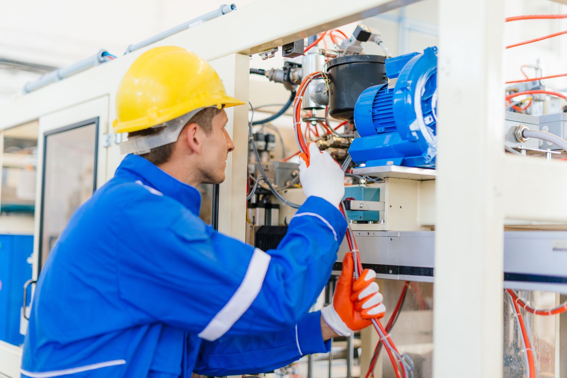 Mechanic in blue jumpsuit and yellow hard hat inspecting machinery.