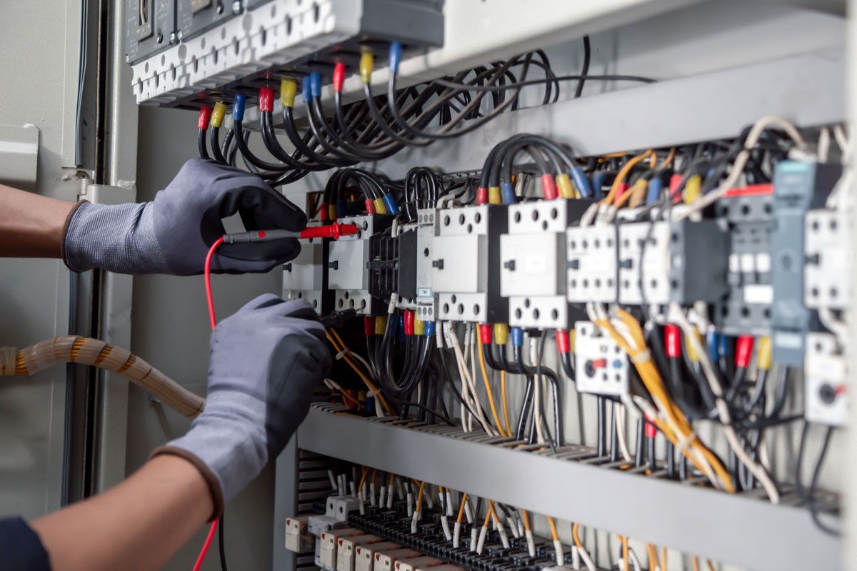 Electrician testing wires inside an electrical panel, wearing gloves. Wires are multi-colored.