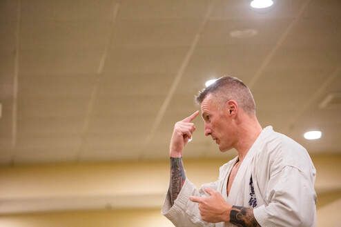 A man in a karate uniform is pointing at his forehead.