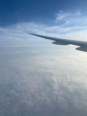 The wing of an airplane is flying in the sky above the clouds.