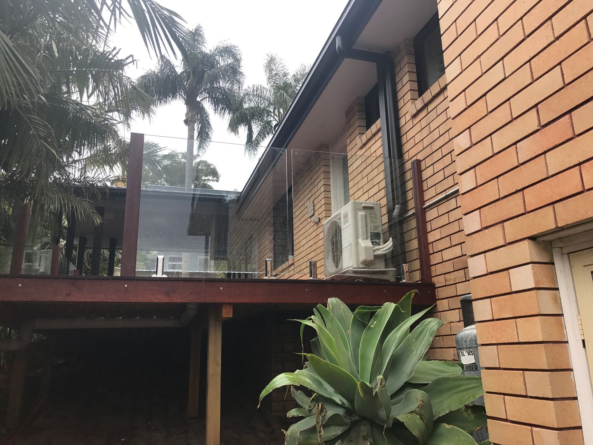 Brick House With a Wooden Deck, Palm Trees, and an Air Conditioner Unit — Keystone Property Solutions In Maitland, NSW